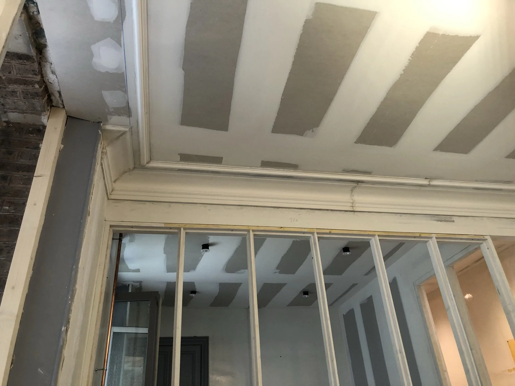 Travaux de rénovation en cours dans une pièce, murs et plafond en cours de finition, structures en bois visibles pour une cloison, éclairage encastré non installé.