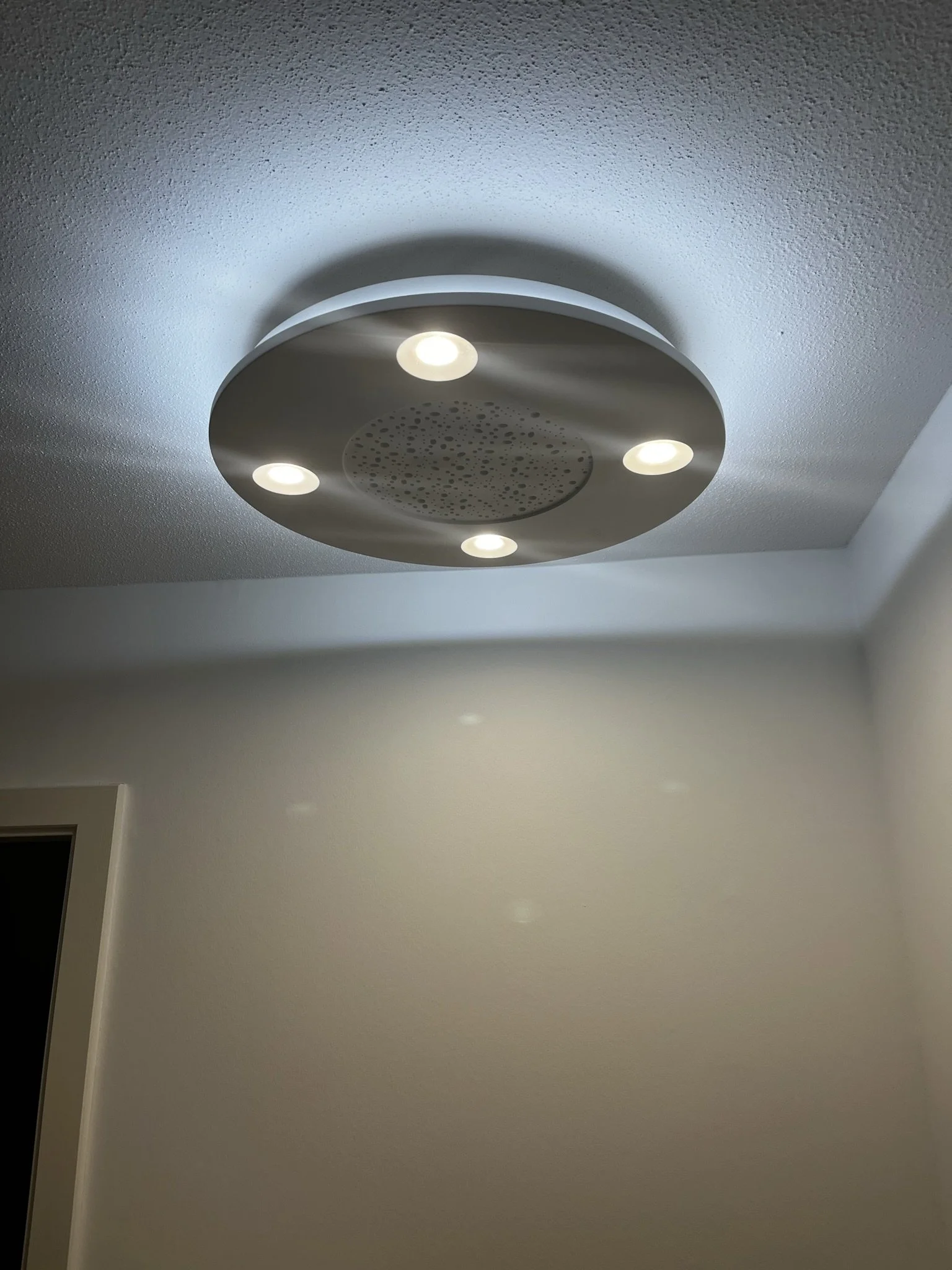 Plafonnier moderne en plâtre avec quatre lumières encastrées dans un plafond suspendu, éclairant une pièce.