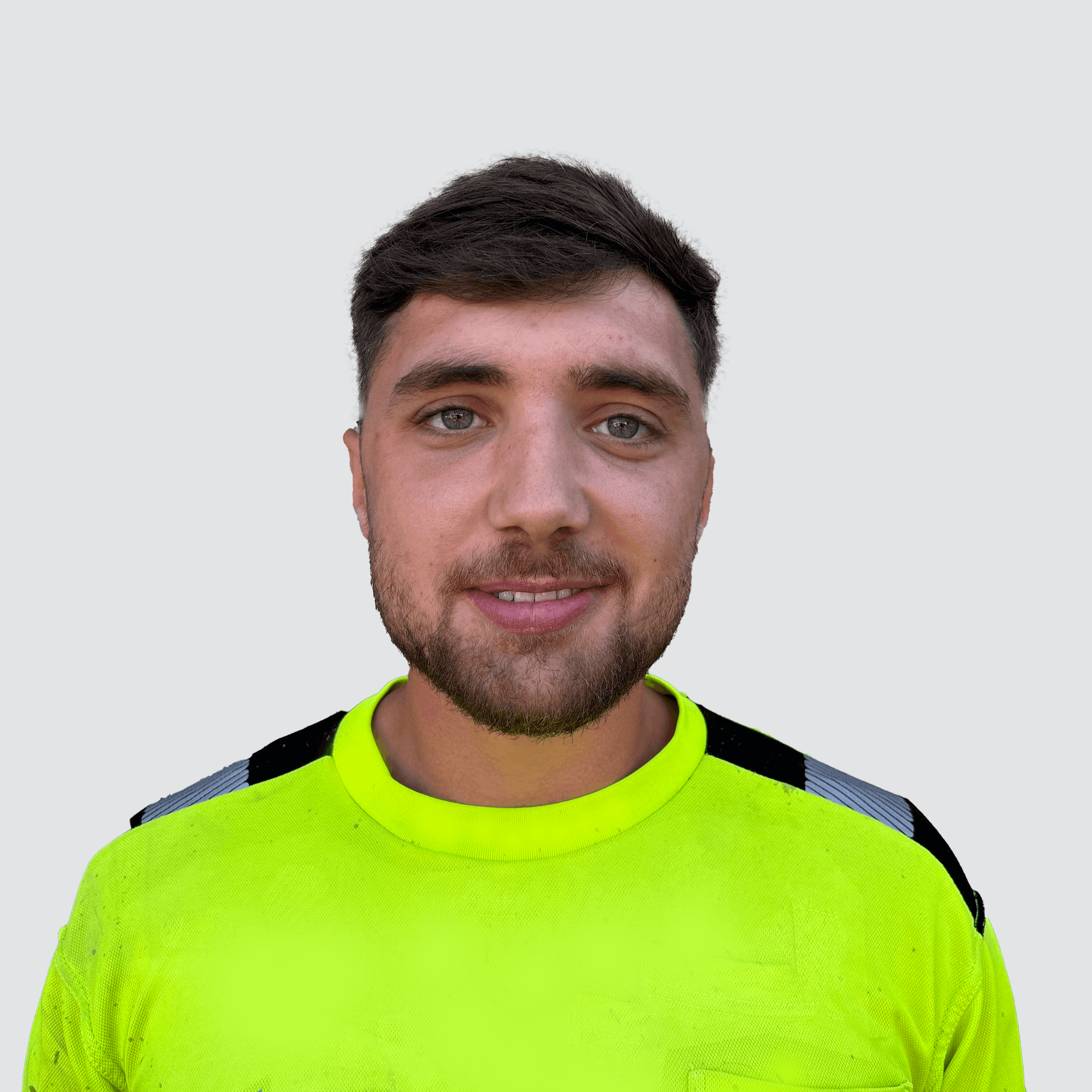 Portrait of a young man with short dark hair, blue eyes, and a beard, wearing a neon yellow sports jersey with black and gray accents on the shoulders, set against a plain light gray background.