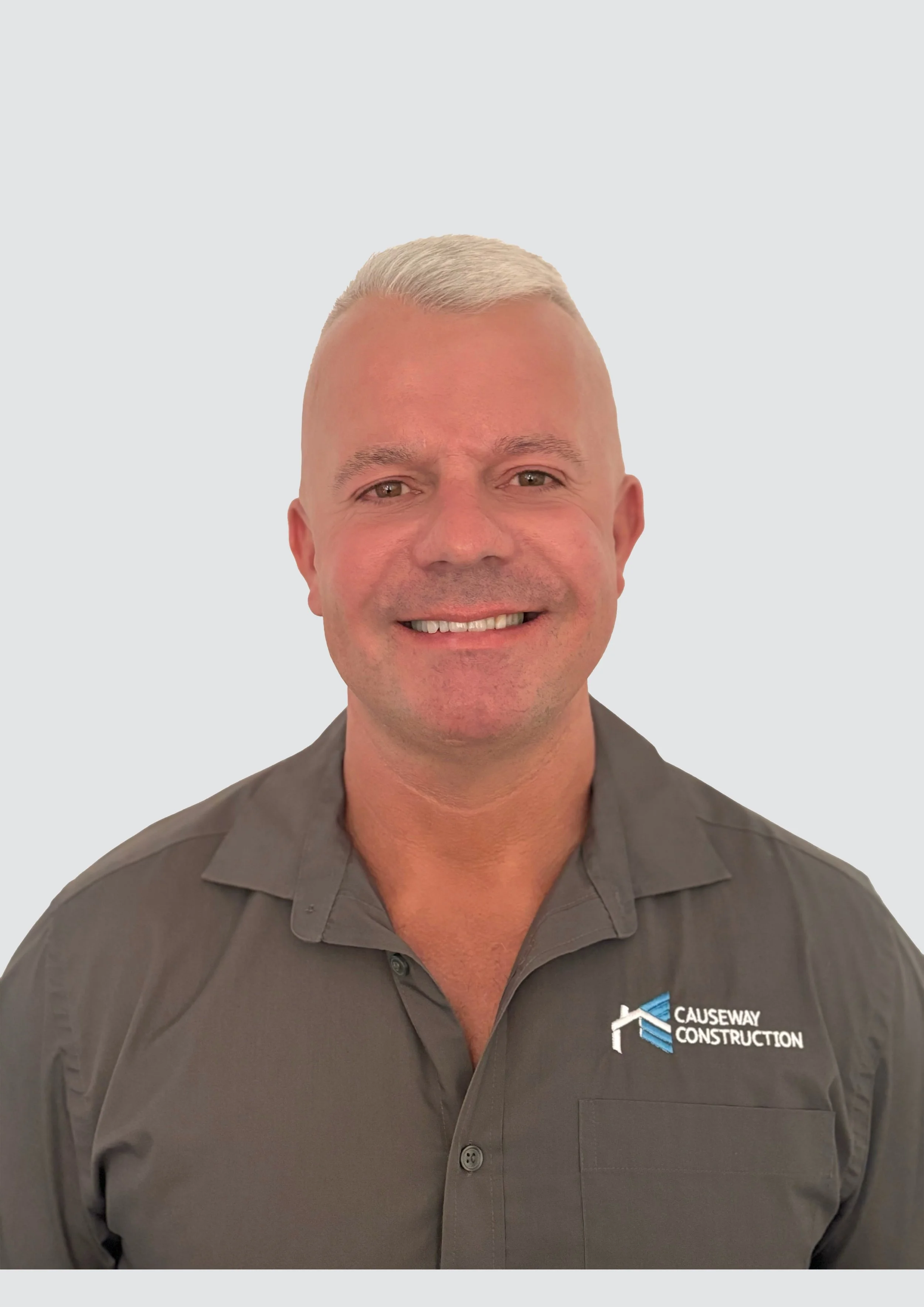 A man smiling, wearing a gray shirt with a 'Causeway Construction' logo, standing against a plain light background.
