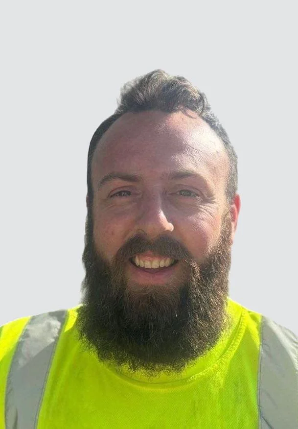 A smiling man with a full beard wearing a bright yellow safety vest.