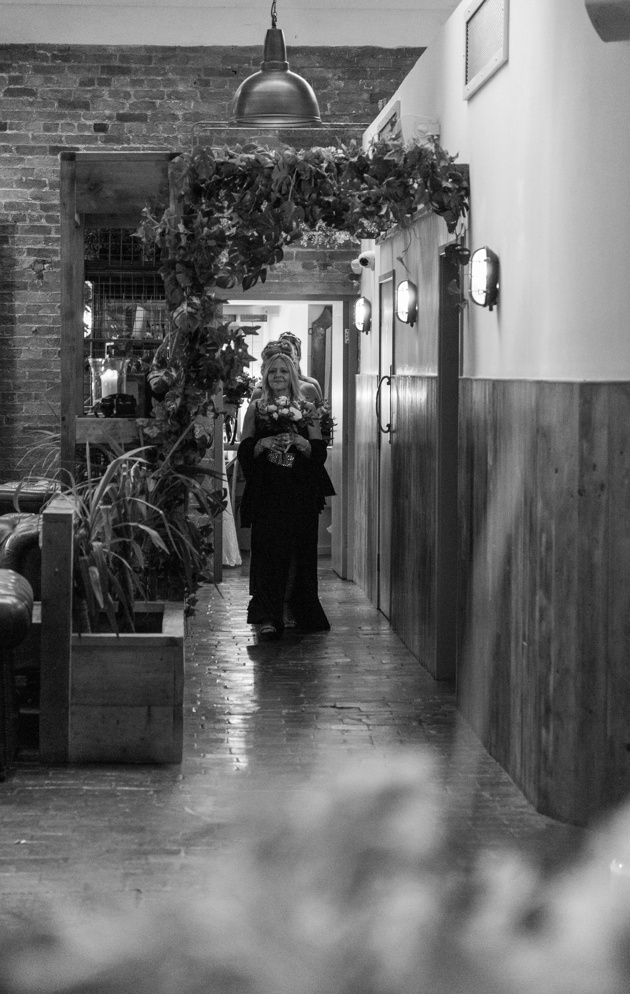A woman in a black dress walking through a decorated restaurant corridor with floral and foliage decorations.