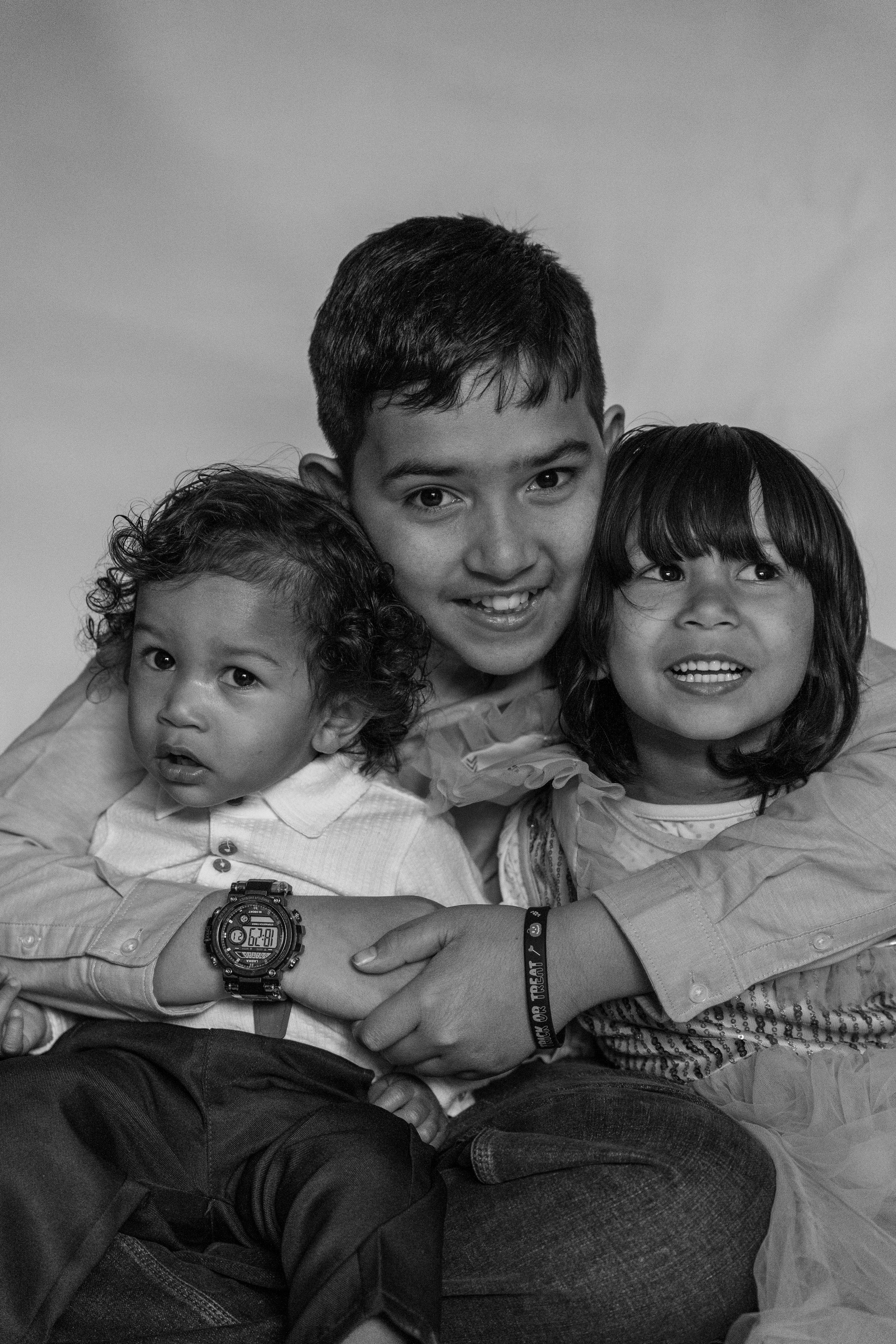 Four children close together, smiling and posing for a photo in a black-and-white image. They are wearing casual clothes and showing various facial expressions.