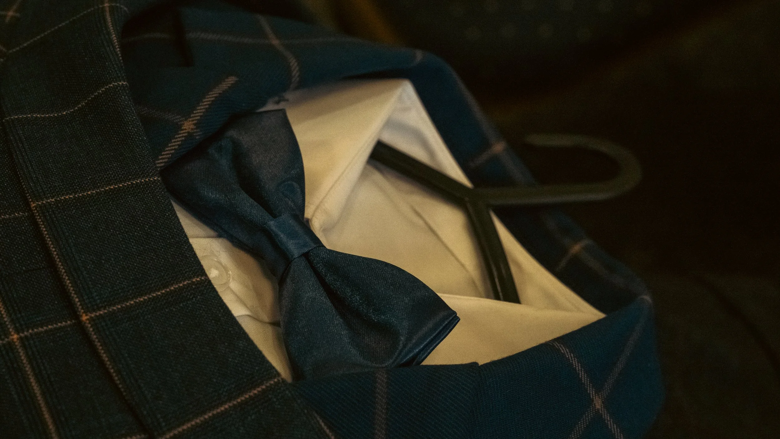 Close-up of a person's lap and seating in a vehicle, showing part of a dark plaid shirt, a dark tie, and a beige seat with black seatbelt.