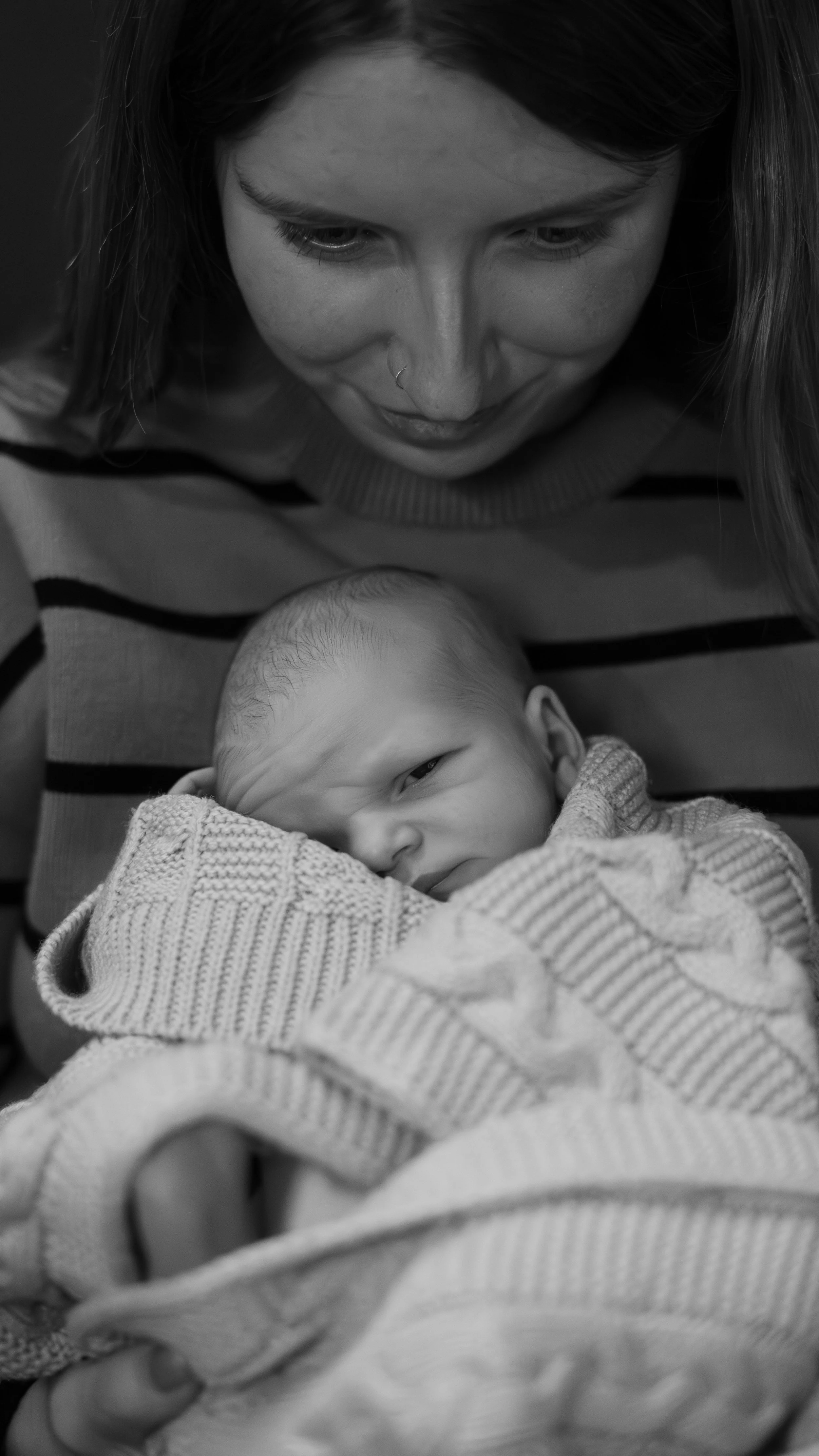 Close-up of a woman looking down at a newborn baby wrapped in a blanket.