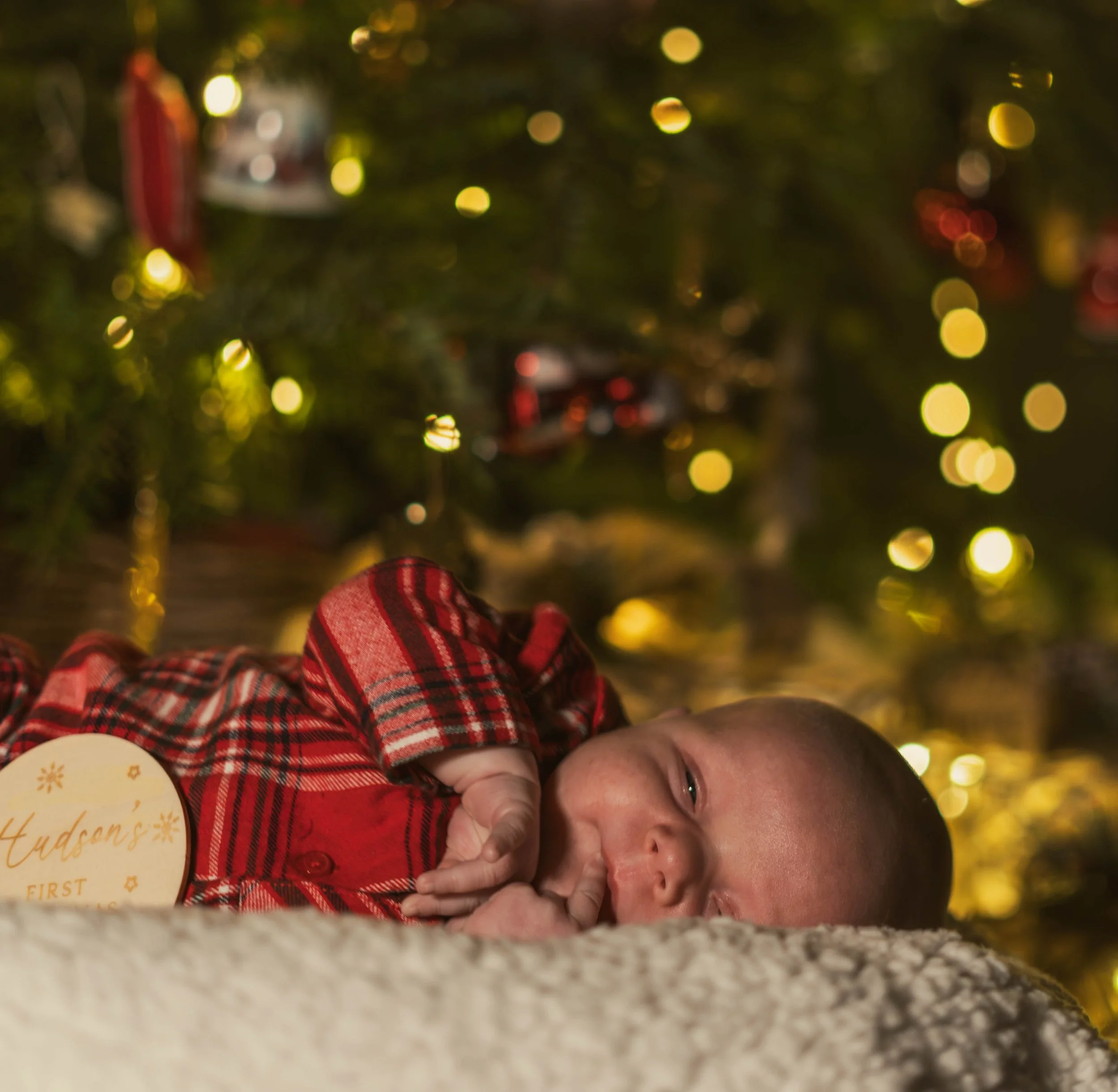 People lying on the floor under a Christmas tree decorated with ornaments and lights.