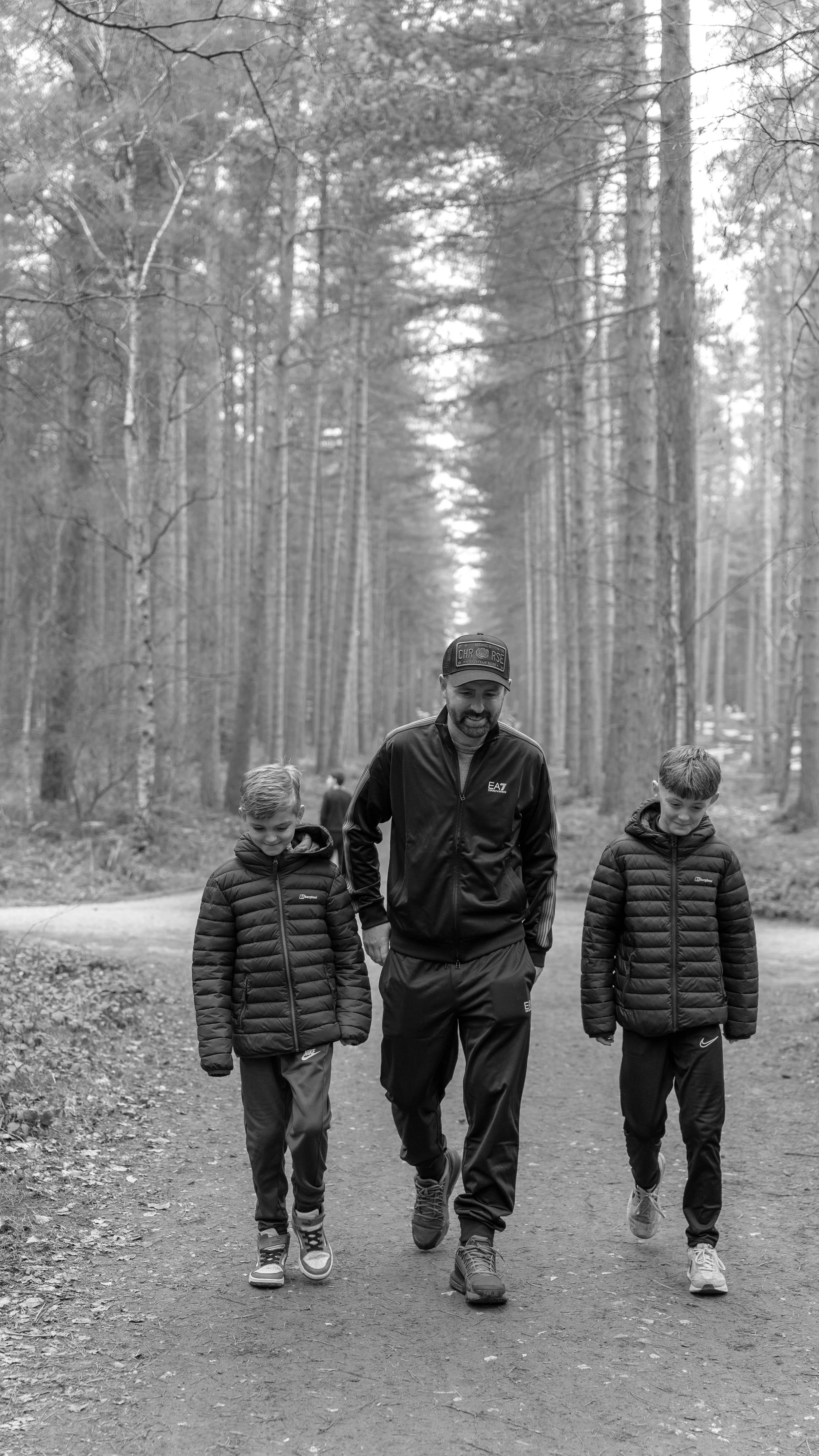 A man walking with two young boys on a forest trail.