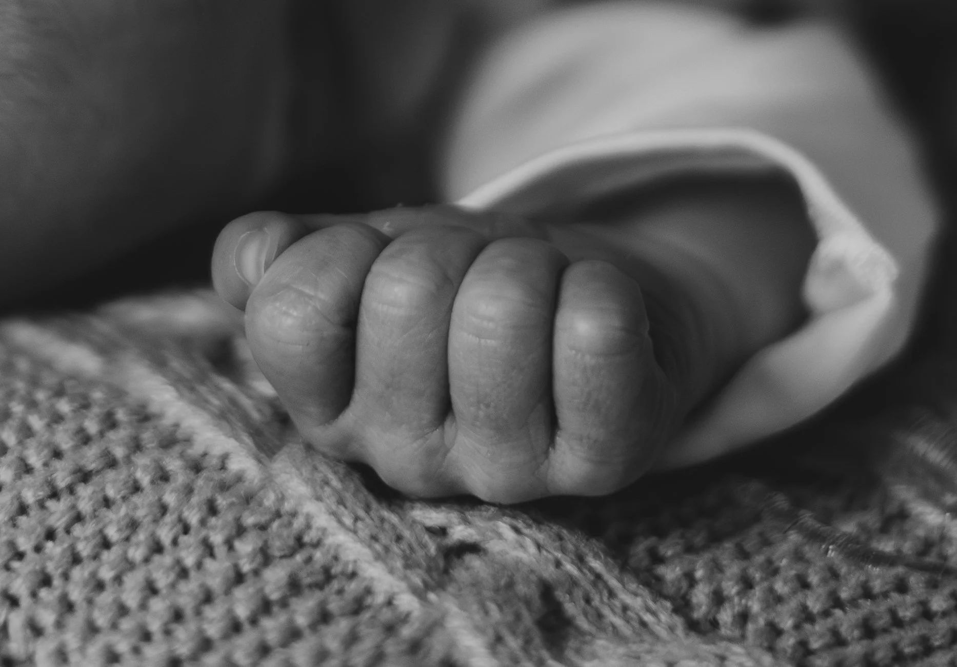 Close-up black and white photo of a hand gripping the edge of cloth or fabric, with textured surface.