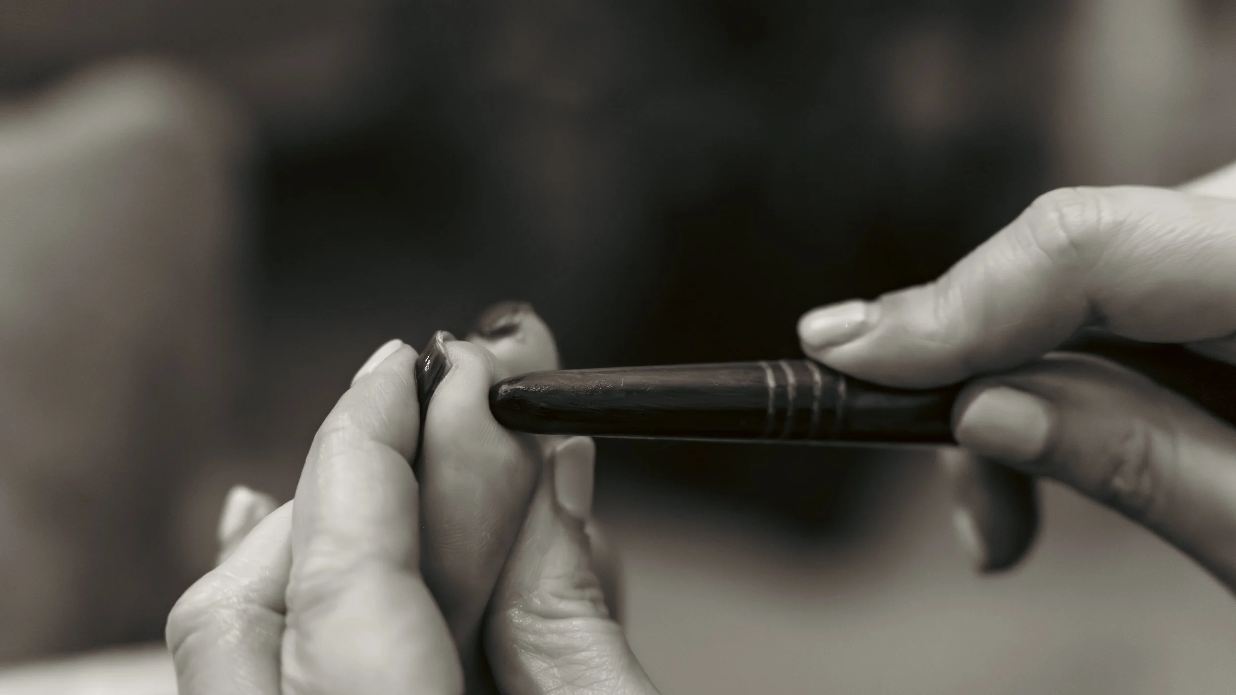 Close-up black-and-white photo of hands holding and examining a small object, possibly an art tool or instrument.