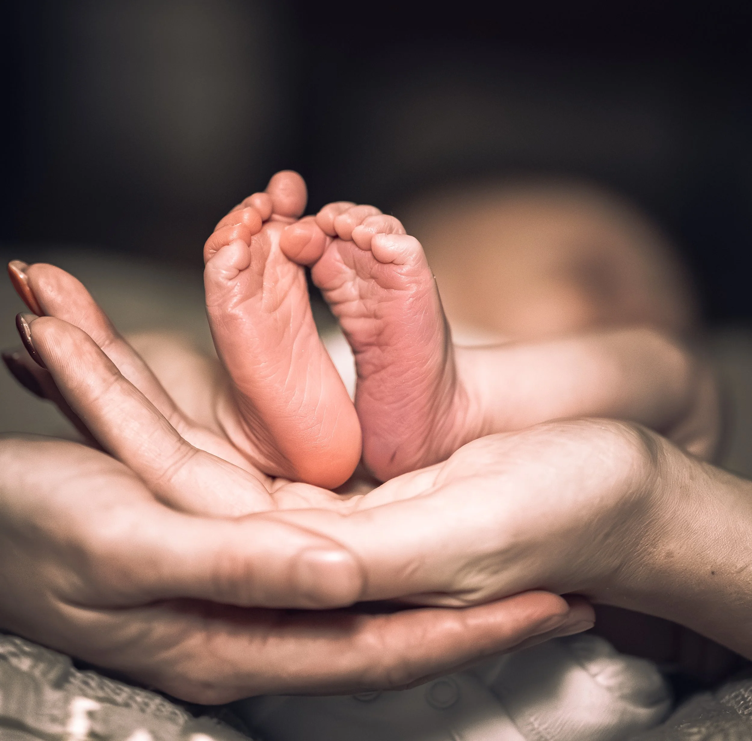 Close-up of a baby's hand being gently held by adult fingers, with a blurred background.