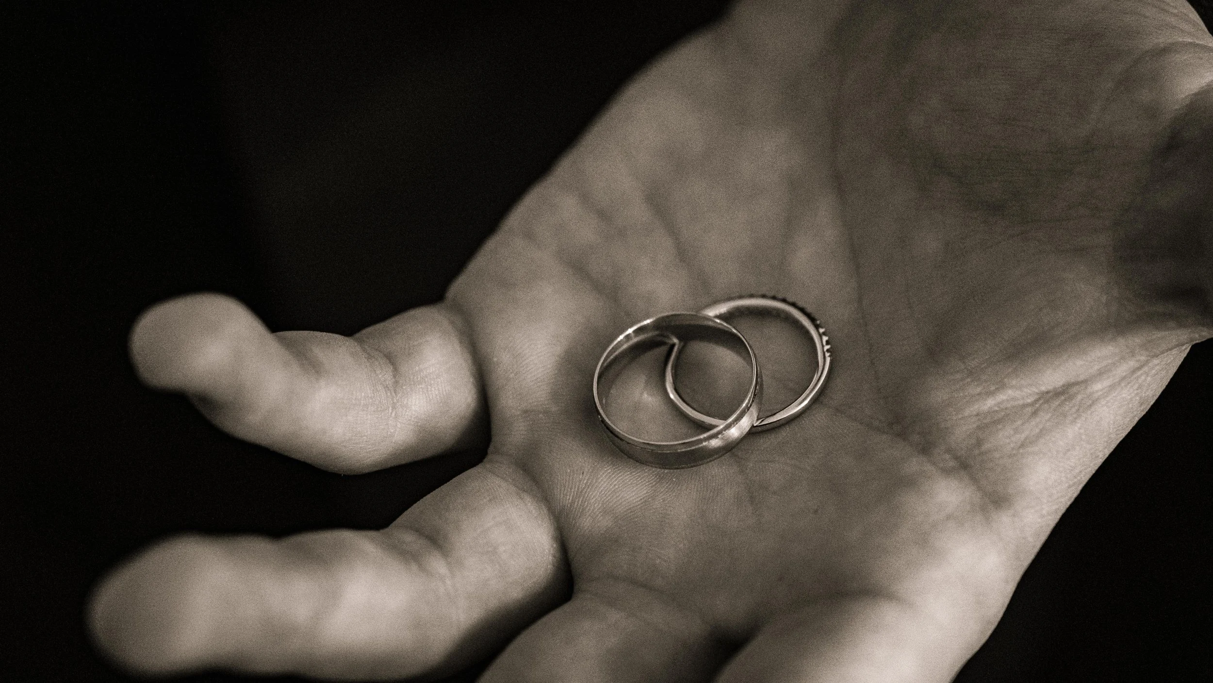 Black and white photo of a hand holding two wedding rings.