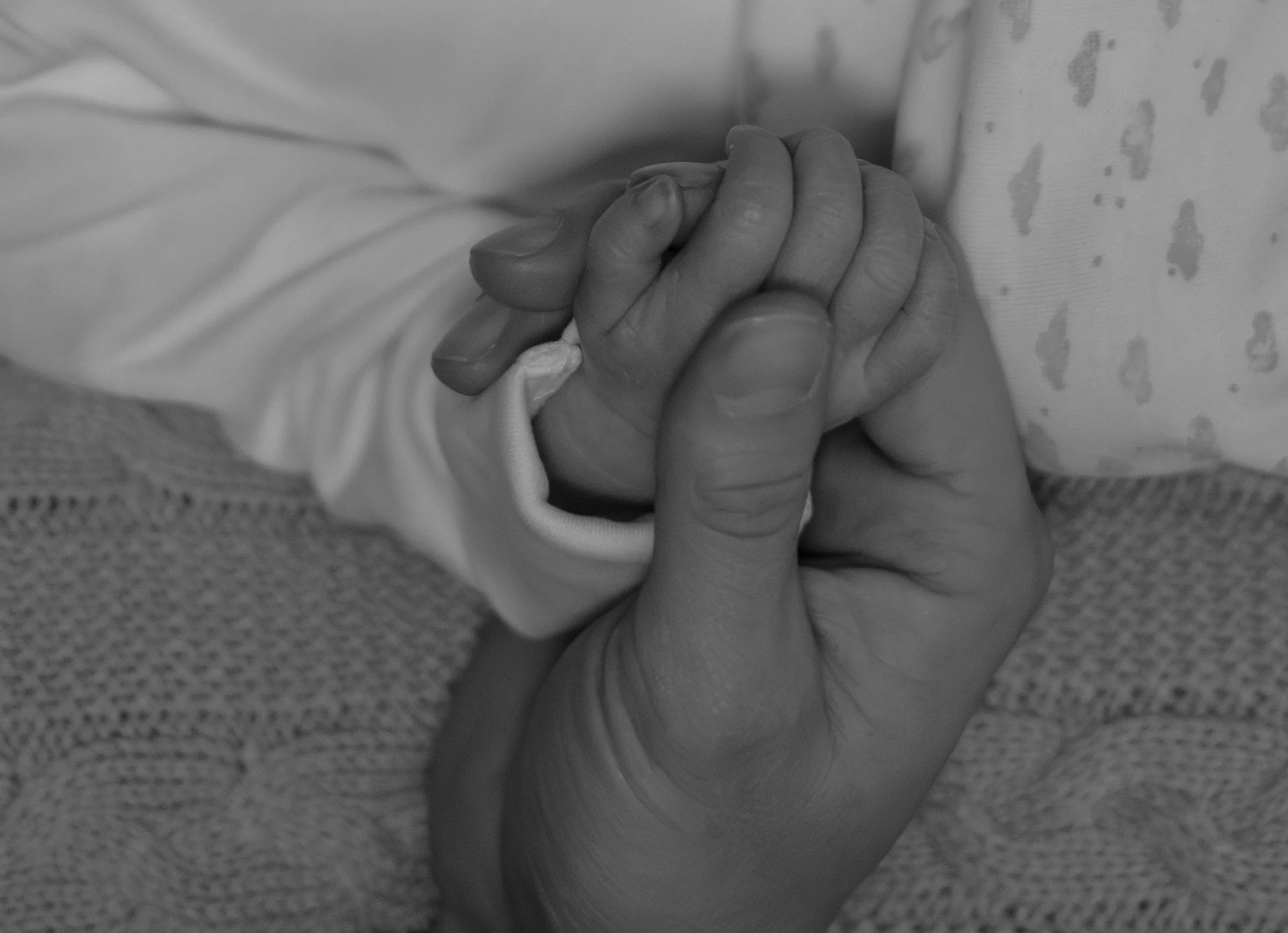 Close-up of an adult hand holding a baby's hand, both hands intertwined.