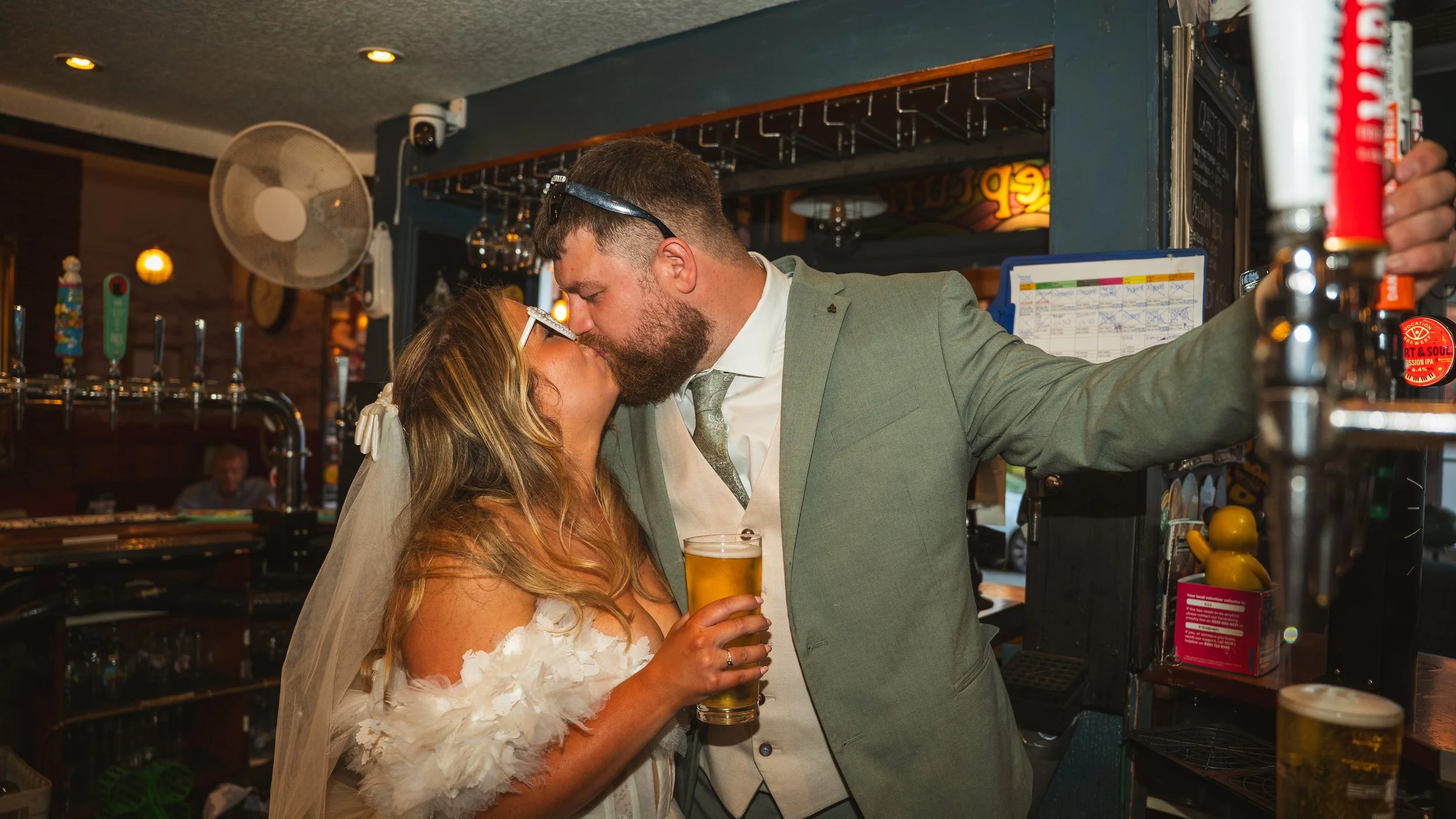 A couple kissing at a bar, with the woman holding a glass of beer.