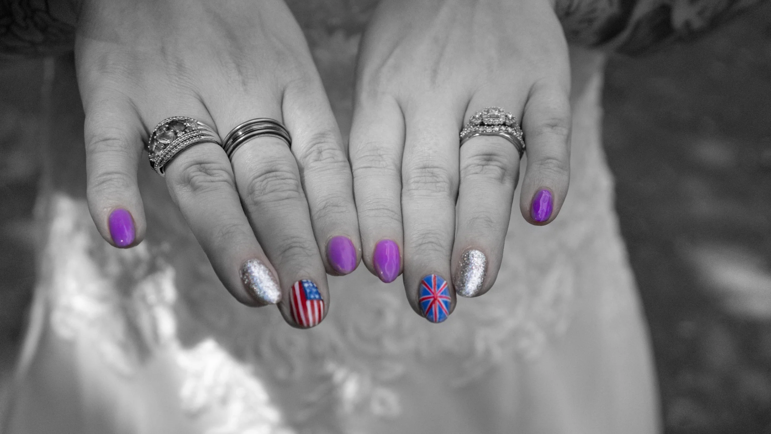 Hands with rings and painted nails, some displaying American and British flags. The image is in black and white, except for the nails which are in color.