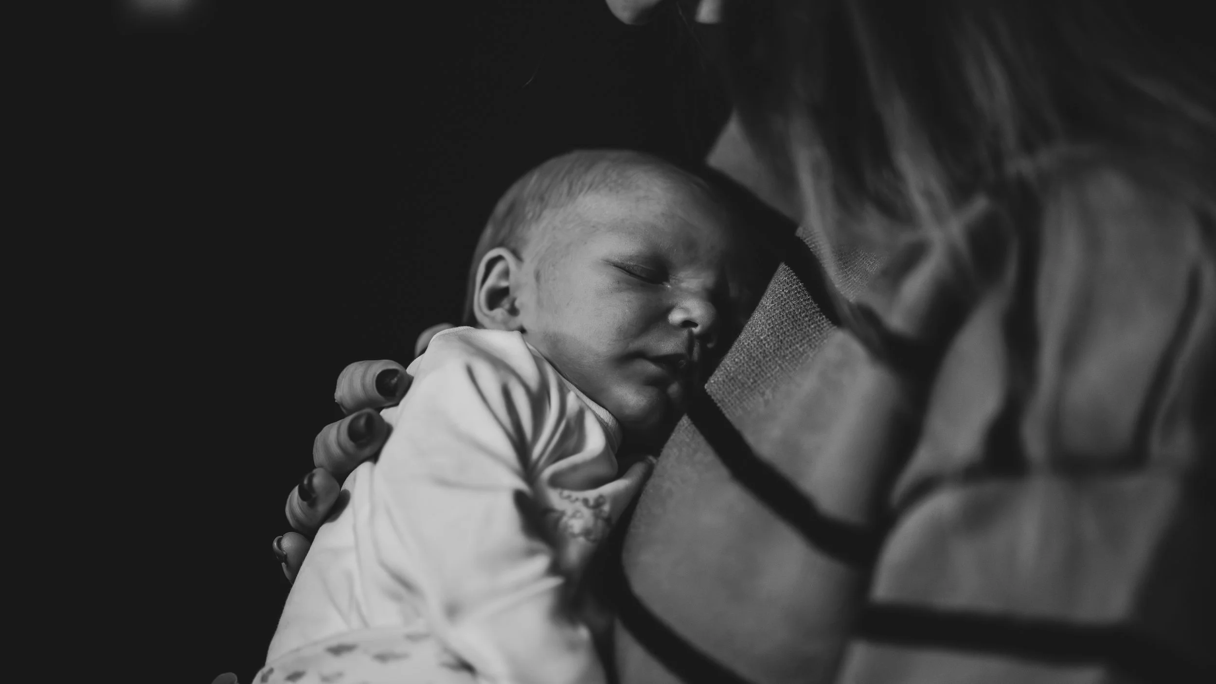 A young child is sleeping peacefully on an adult's shoulder, with their face close to the adult's neck. The adult is gently holding the child, providing comfort and security.