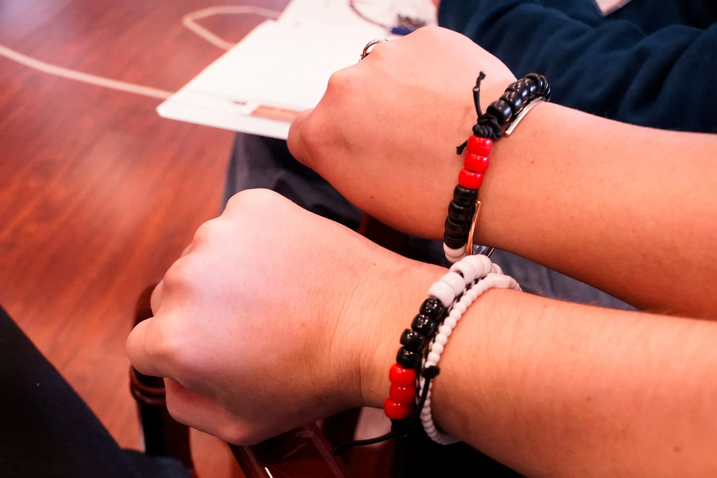 Close-up of multiple wrists wearing black and red beaded bracelets.