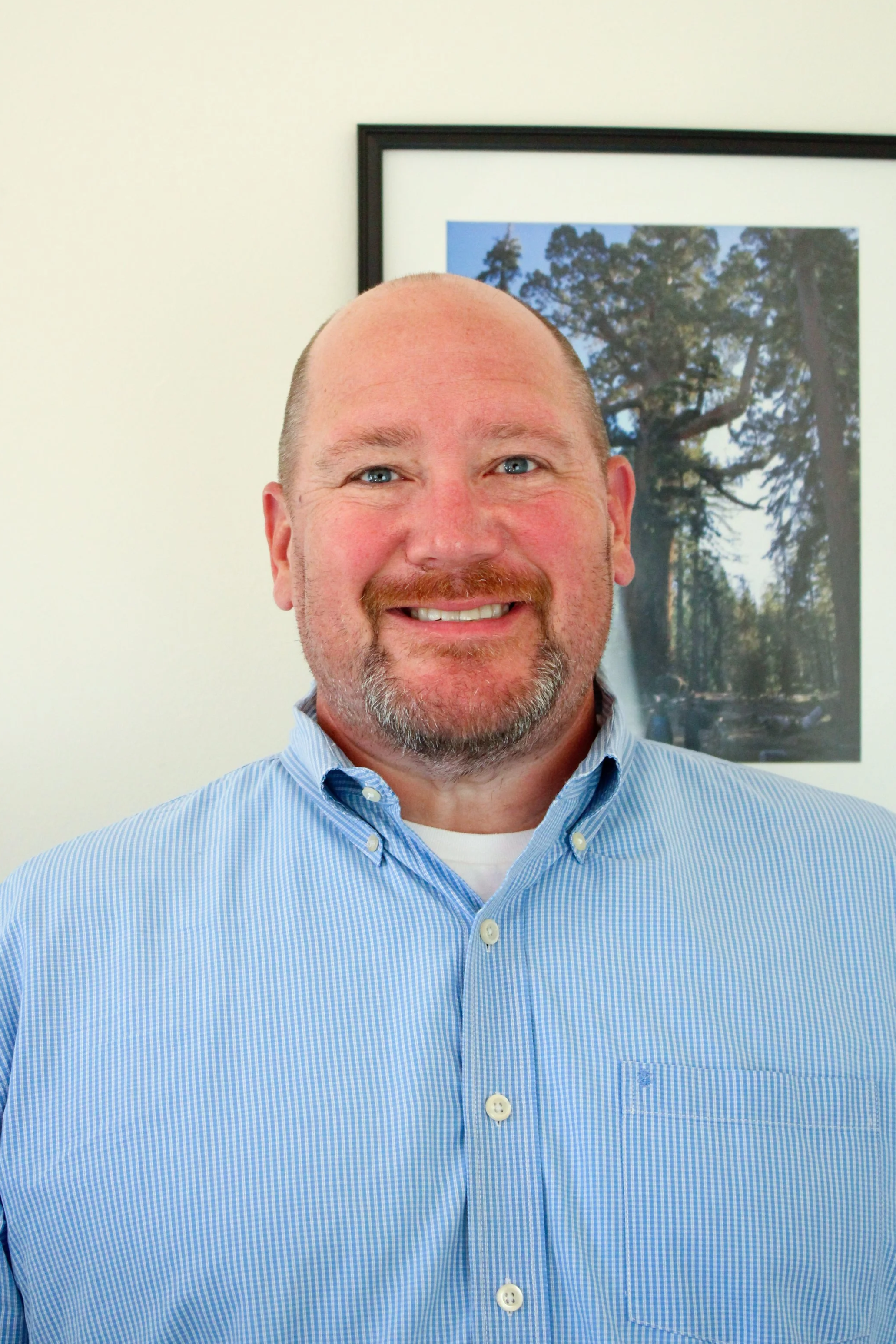 smiling photo of a middle aged man in front of a picture frame