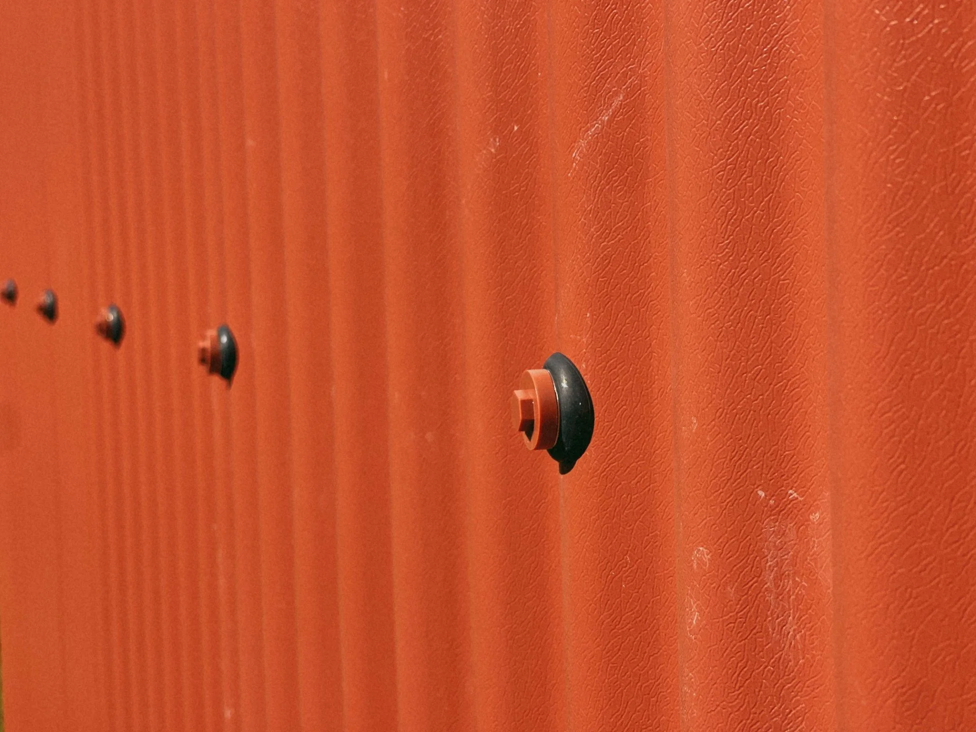 Close-up of a series of black and orange rubber bumpers attached to an orange textured surface, possibly a wall or ceiling.