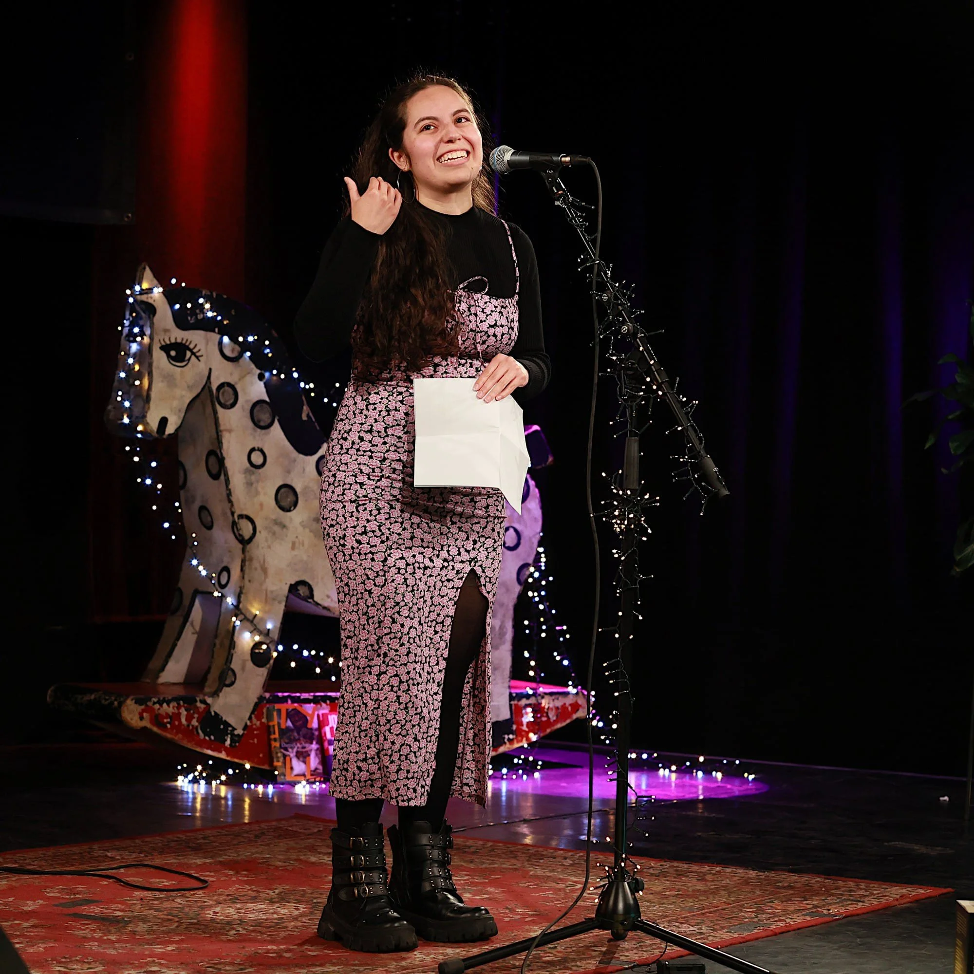 Eine junge Frau steht auf einer Bühne, lächelt und spricht in ein Mikrofon. Sie nimmt an einem Poetry Slam teil.