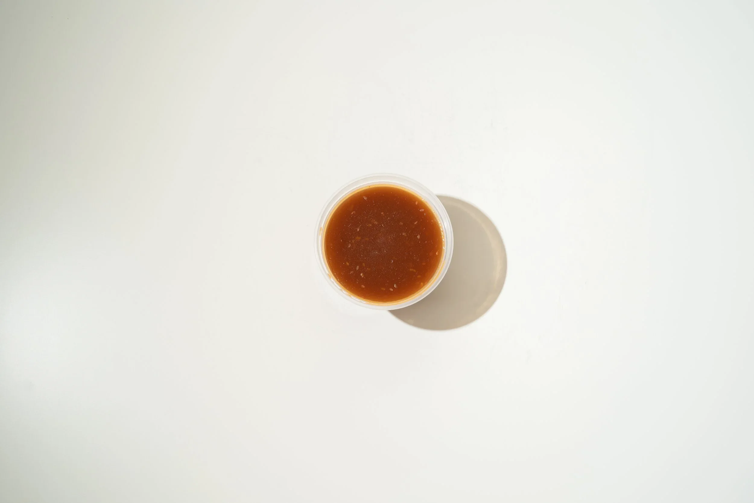 Top-down view of a cup of brown liquid on a white surface, casting a shadow.