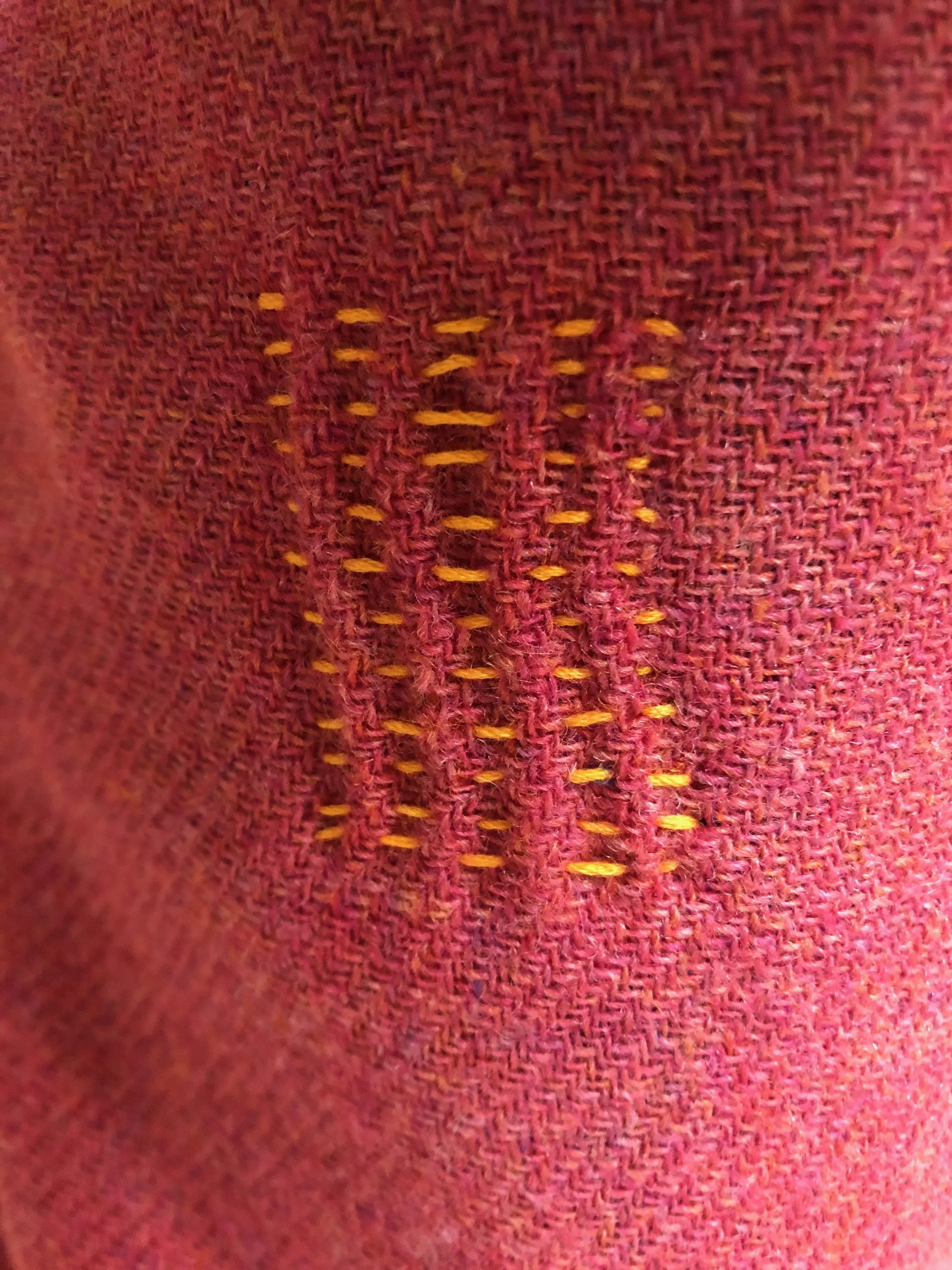 Close-up of red fabric with yellow stitches forming a 'W' shape.