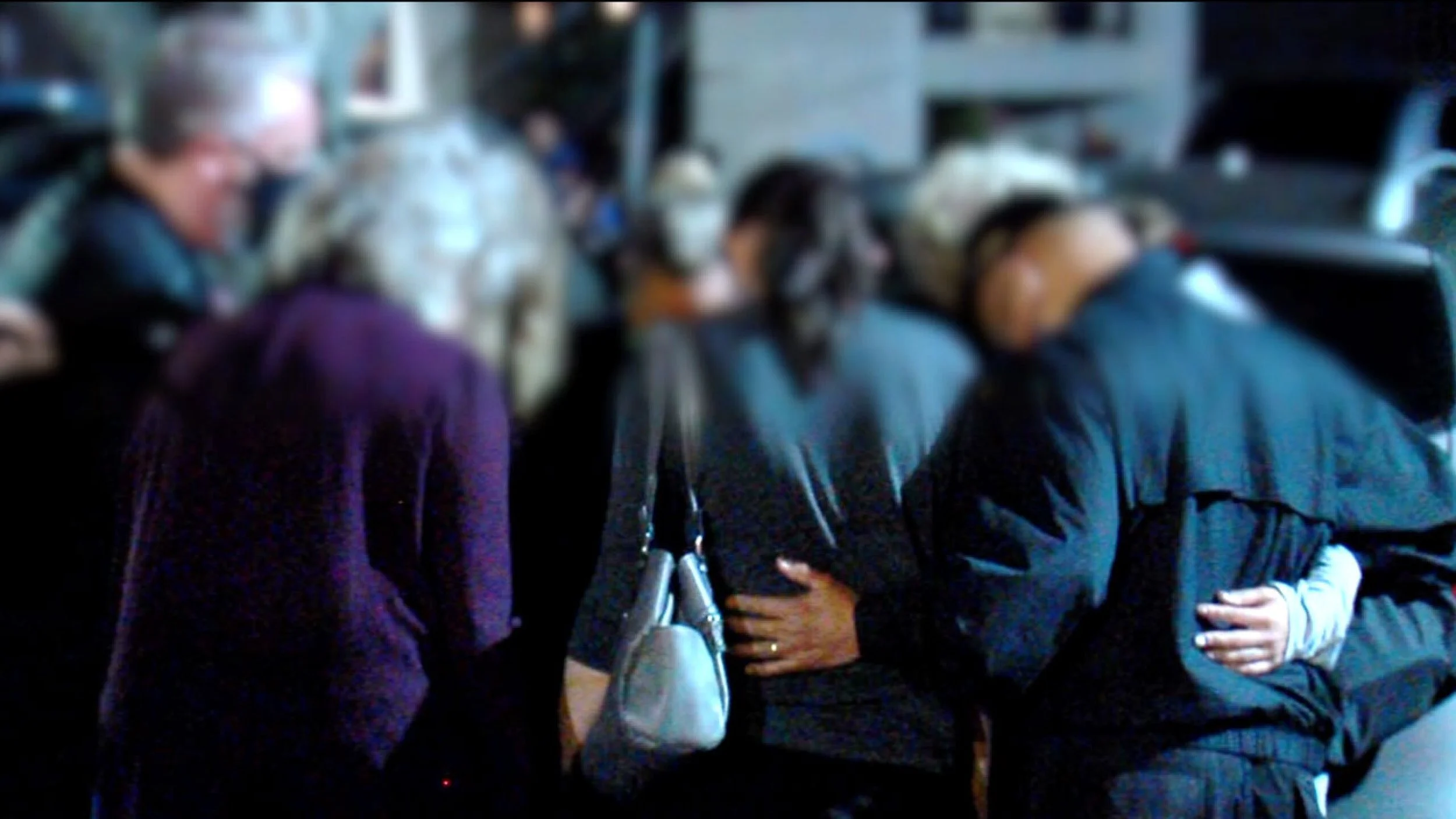 Group of people praying outside, with their heads bowed and hands on each other's backs.