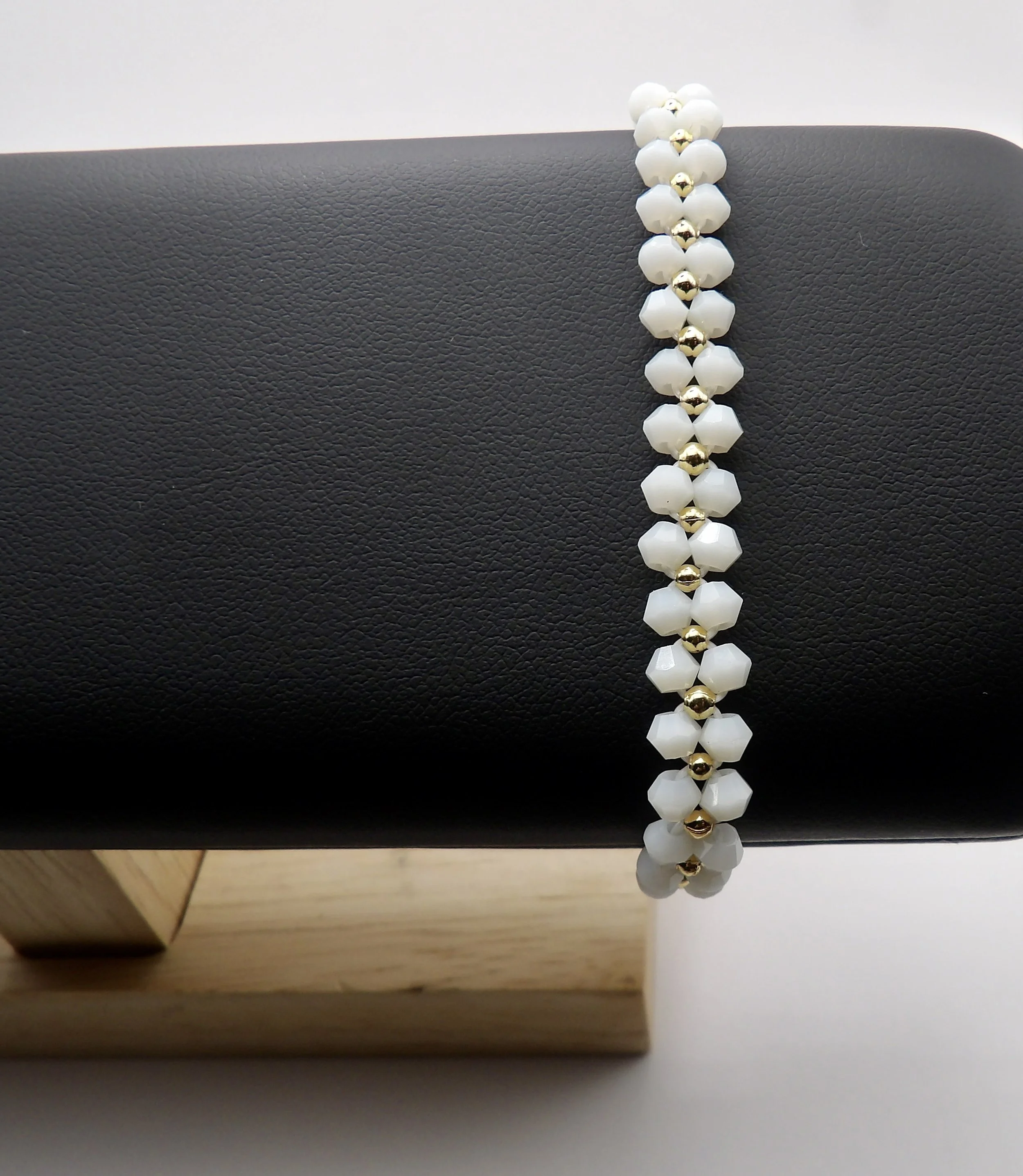 handmade woven bracelet featuring white crystal flowers with 18k solid gold centers. intricate cross-weave design.