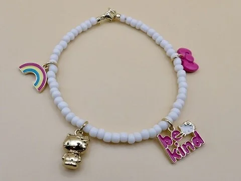 handmade 18k solid gold charm bracelet with 4 sanrio enamel charms (hello kitty, rainbow, bow, be kind) on a dainty white glass bead band.