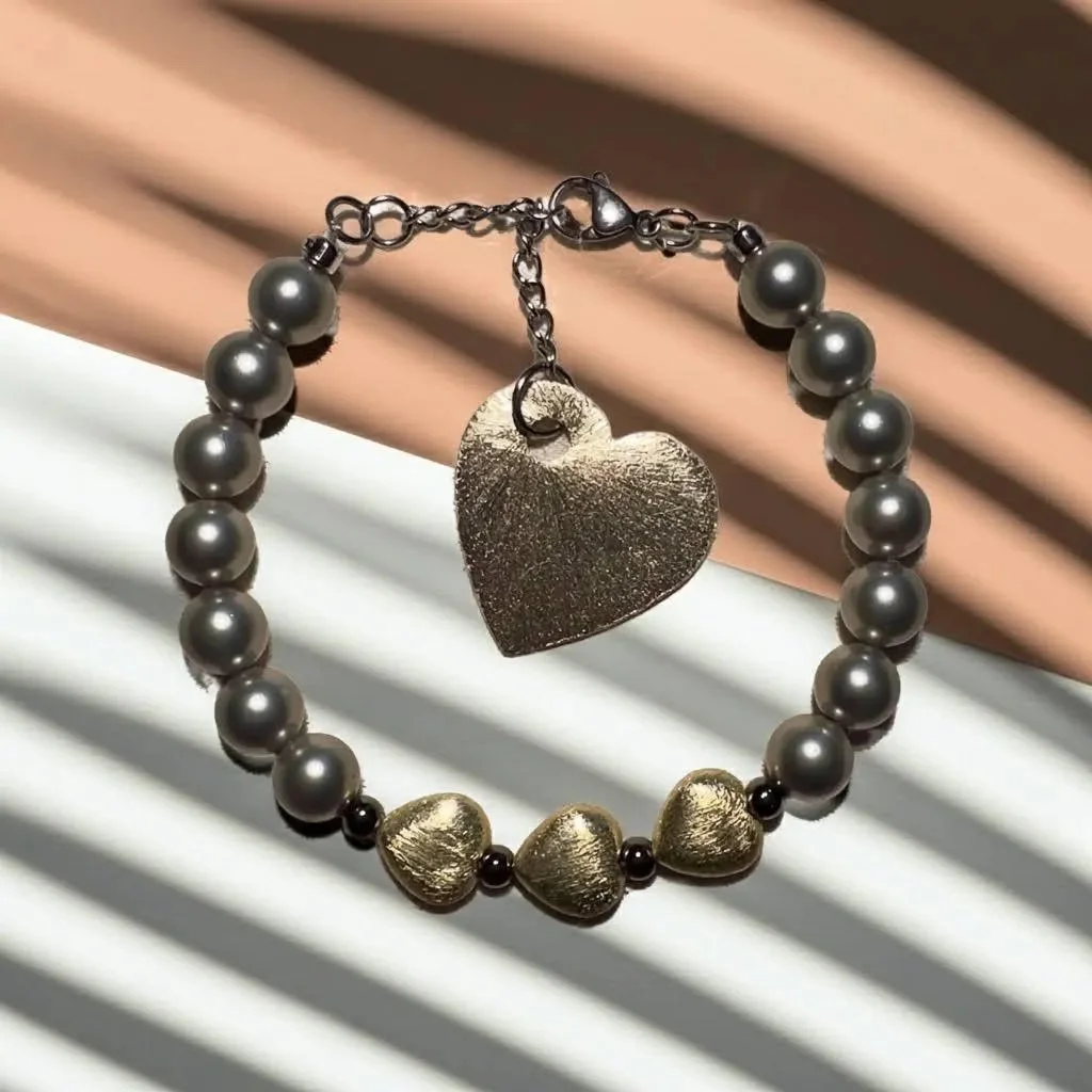 close-up of the dark romantic bracelet highlighting the oil-slick sheen of gunmetal mother of pearl against gold-finished hearts.