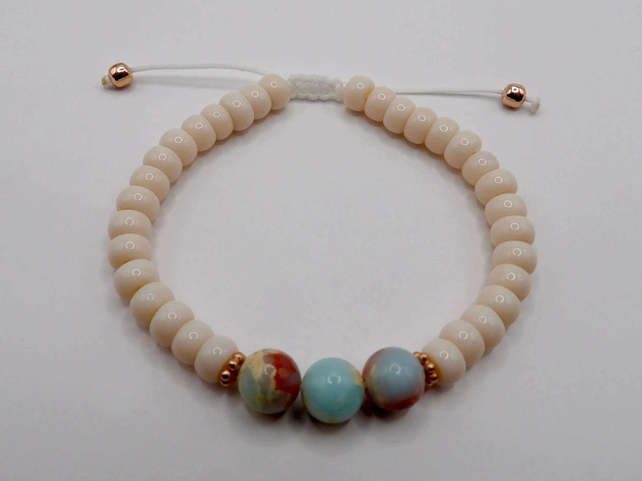 handmade adjustable bracelet featuring cream glass heishi beads, a centerpiece of three 8mm blue african opal beads, and 14k rose gold daisy spacers.
