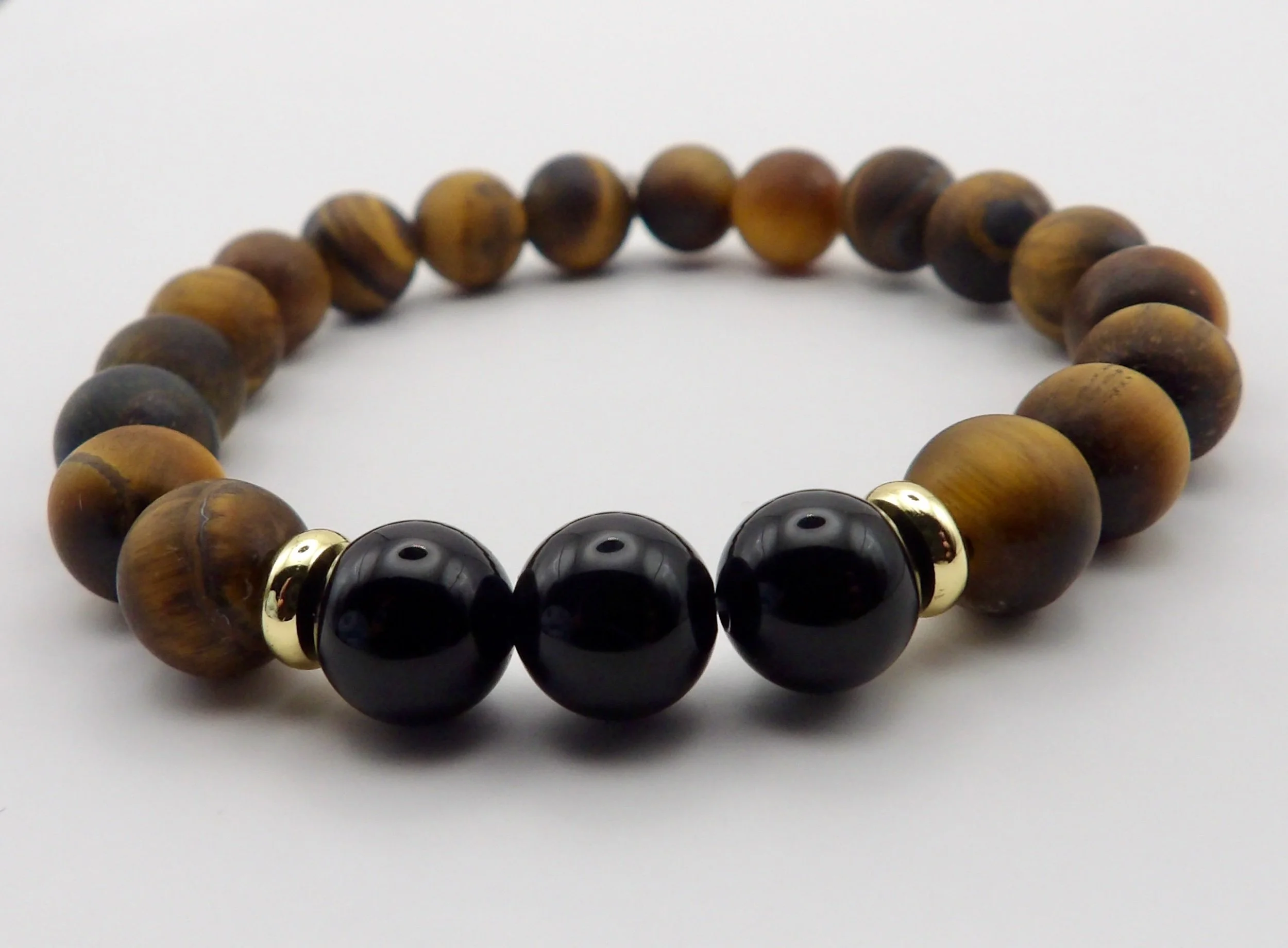 detail of the stretch bracelet with a polished black onyx centerpiece and 18k gold accents on a matte tigers eye band.