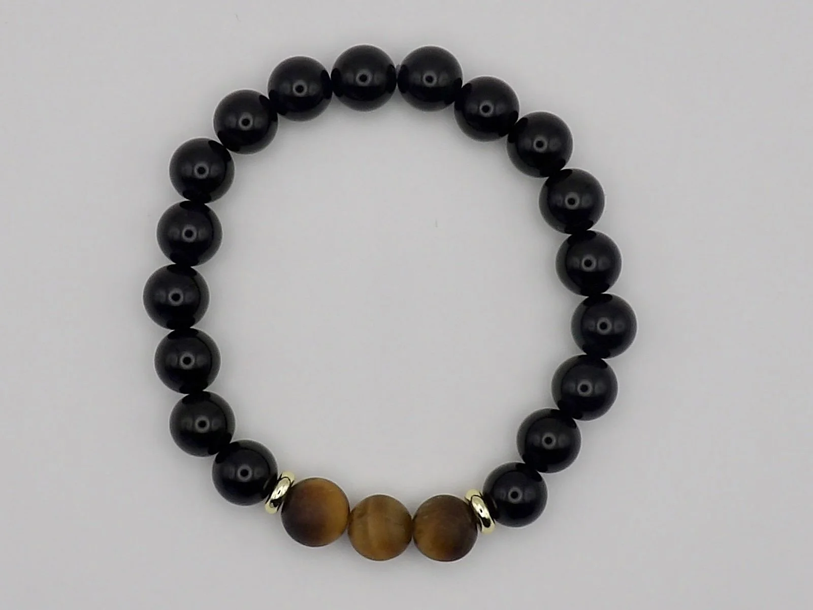 detail of the stretch bracelet with a matte tigers eye centerpiece and 18k gold accents on a polished black onyx band.