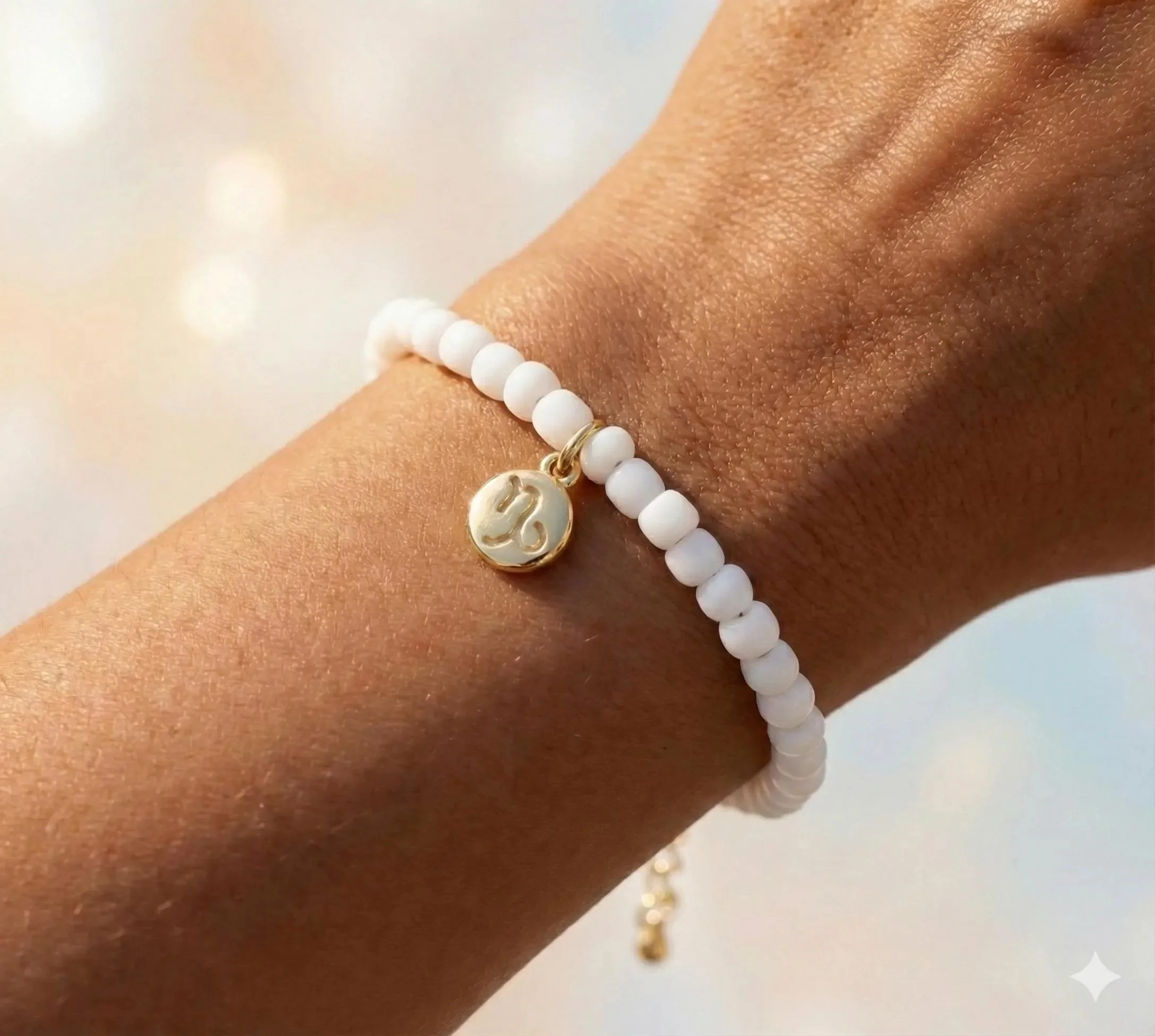 18k gold zodiac charm bracelet on a wrist with dainty white seed beads and gold accents.