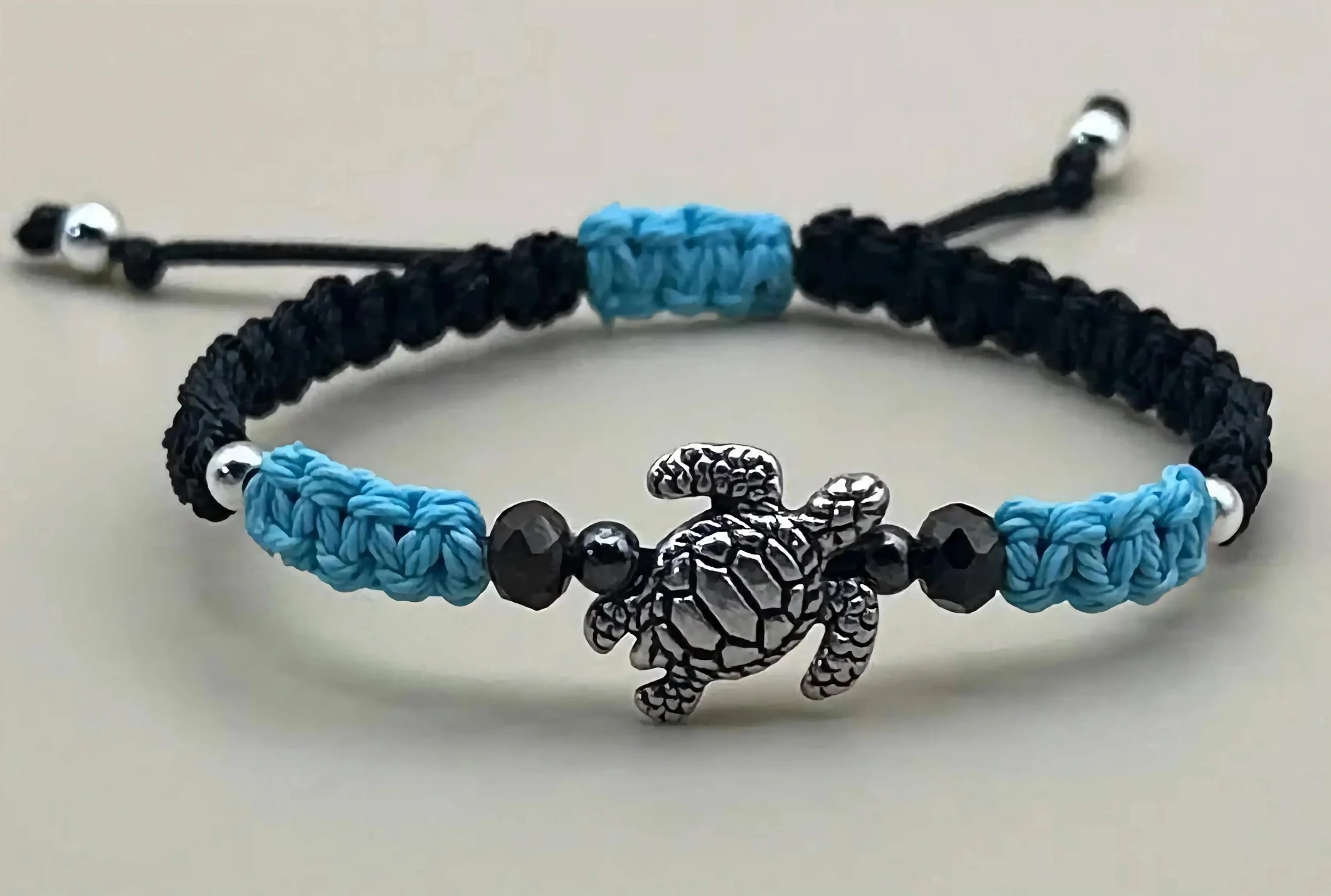 detailed view of the sterling silver turtle charm and the artisan micro-macramé knots in deep sea blue and black.