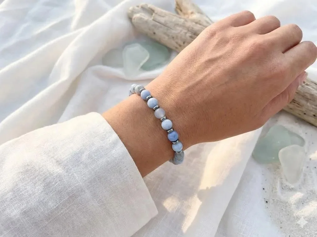 a minimalist, ocean-inspired stretch bracelet showing the natural, cloud-like white banding of blue lace agate alongside mirror-shine platinum discs.