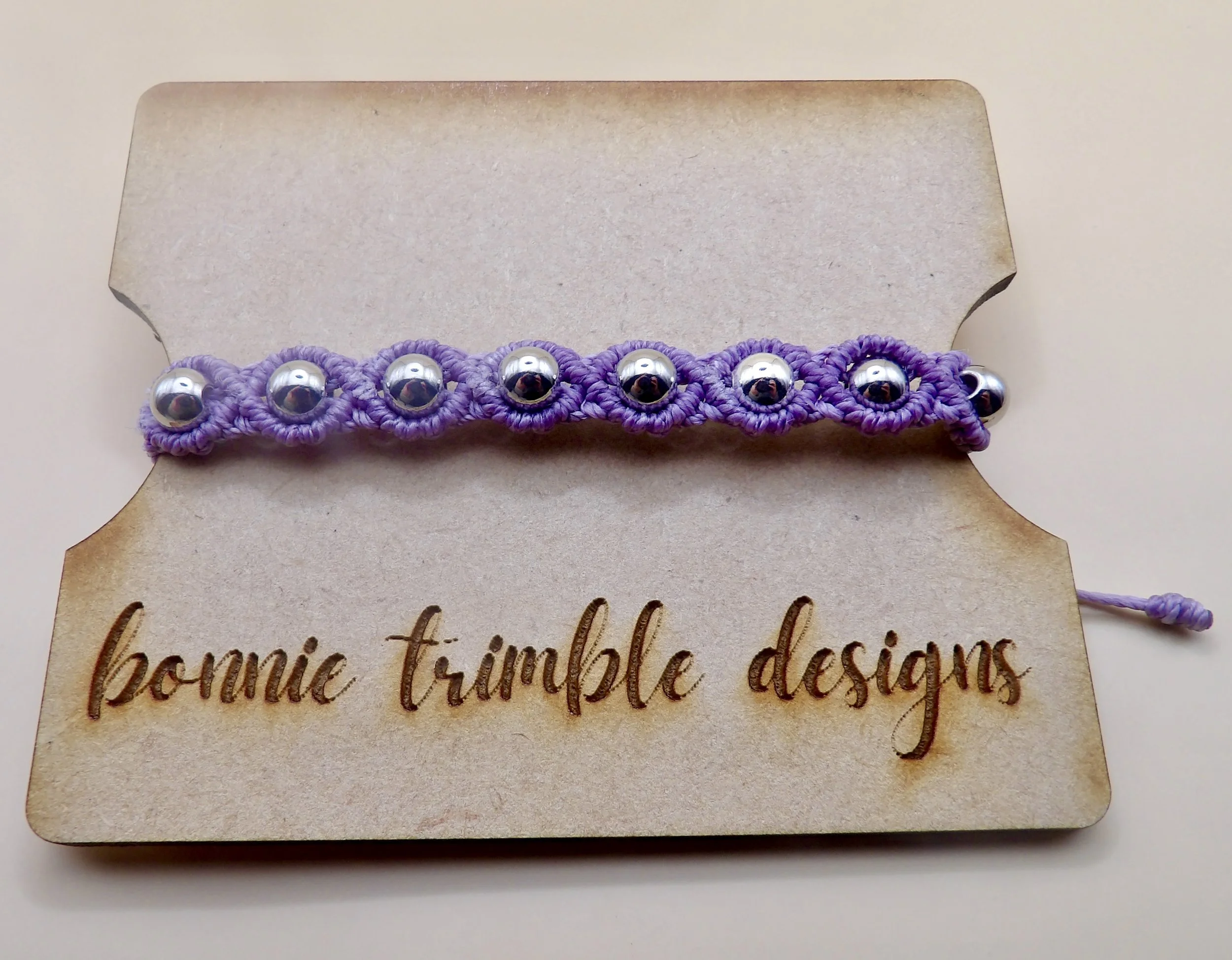 Handmade lilac micro macrame bracelet featuring solid 6mm stainless steel beads woven into a circular pattern. Weighted, adjustable industrial boho jewelry.