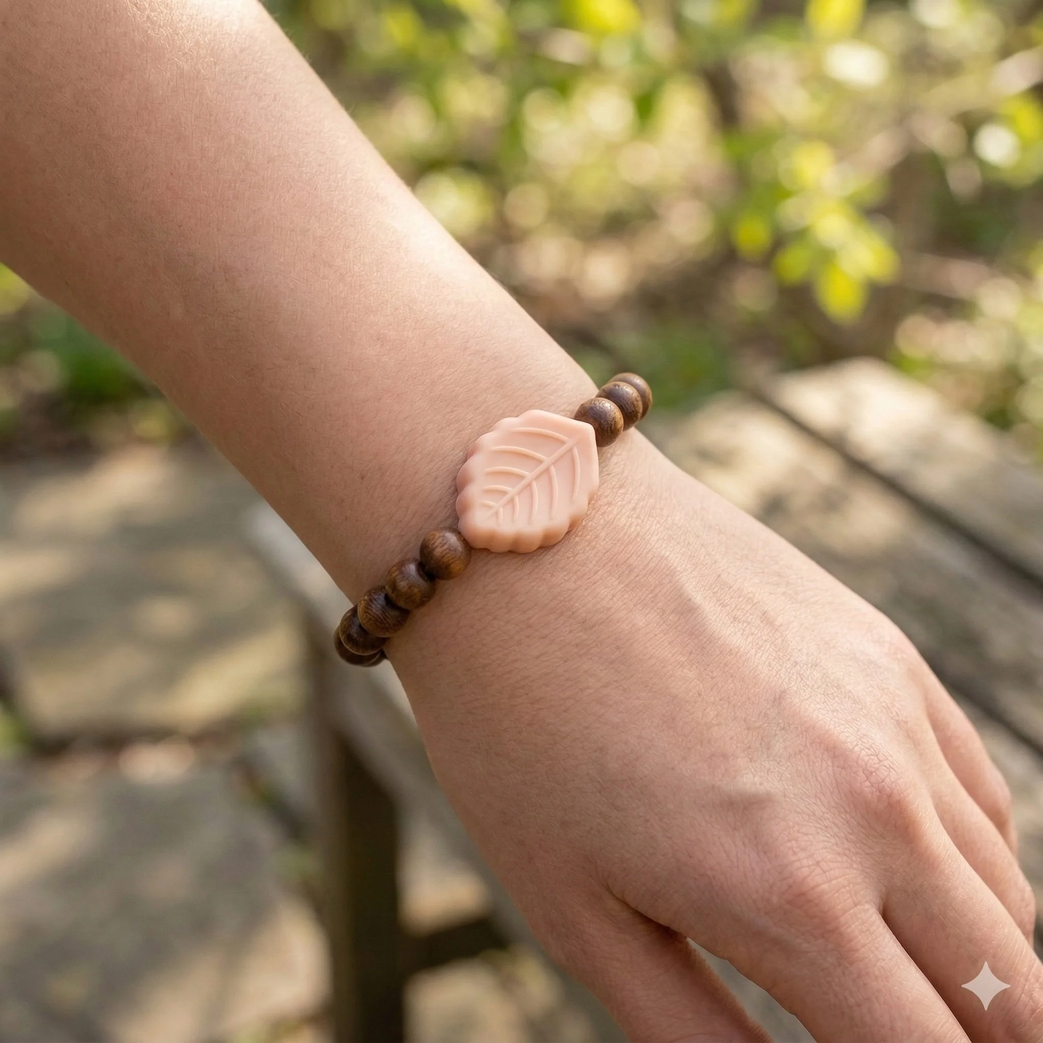tactile peach silicone leaf charm bracelet on a wrist with dark natural wood beads.
