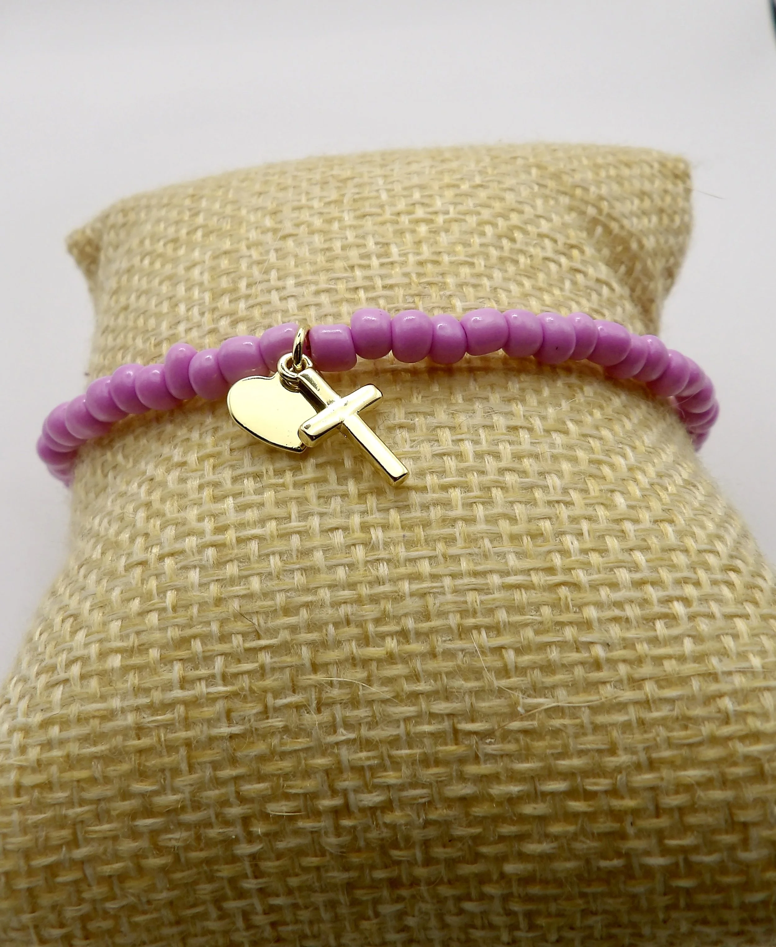 close-up detail of the 18k yellow gold heart and cross charms on the beaded bracelet.