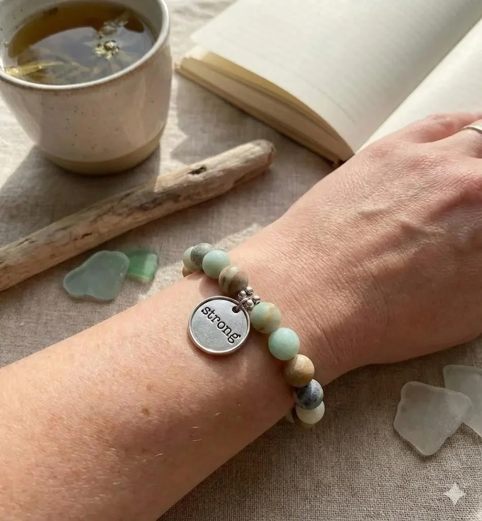 matte amazonite gemstone bracelet on a wrist with a silver inspirational word charm and daisy spacers.