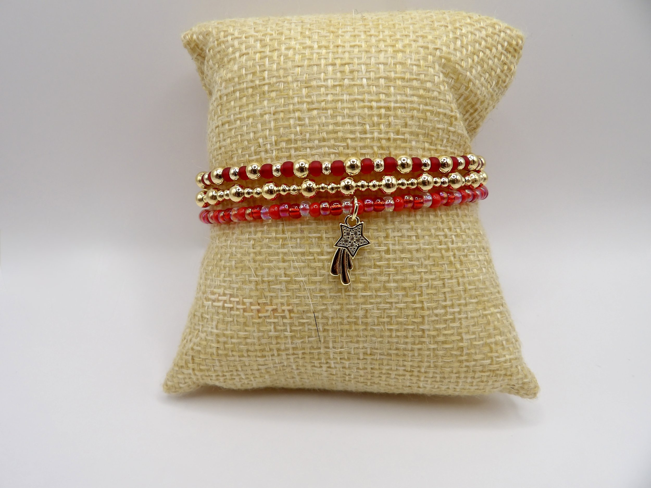 handmade 3-piece 18k solid gold bracelet set stacked, showing a red & gold bead bracelet, an all-gold bead bracelet, and a red bracelet with a pave cz shooting star charm.