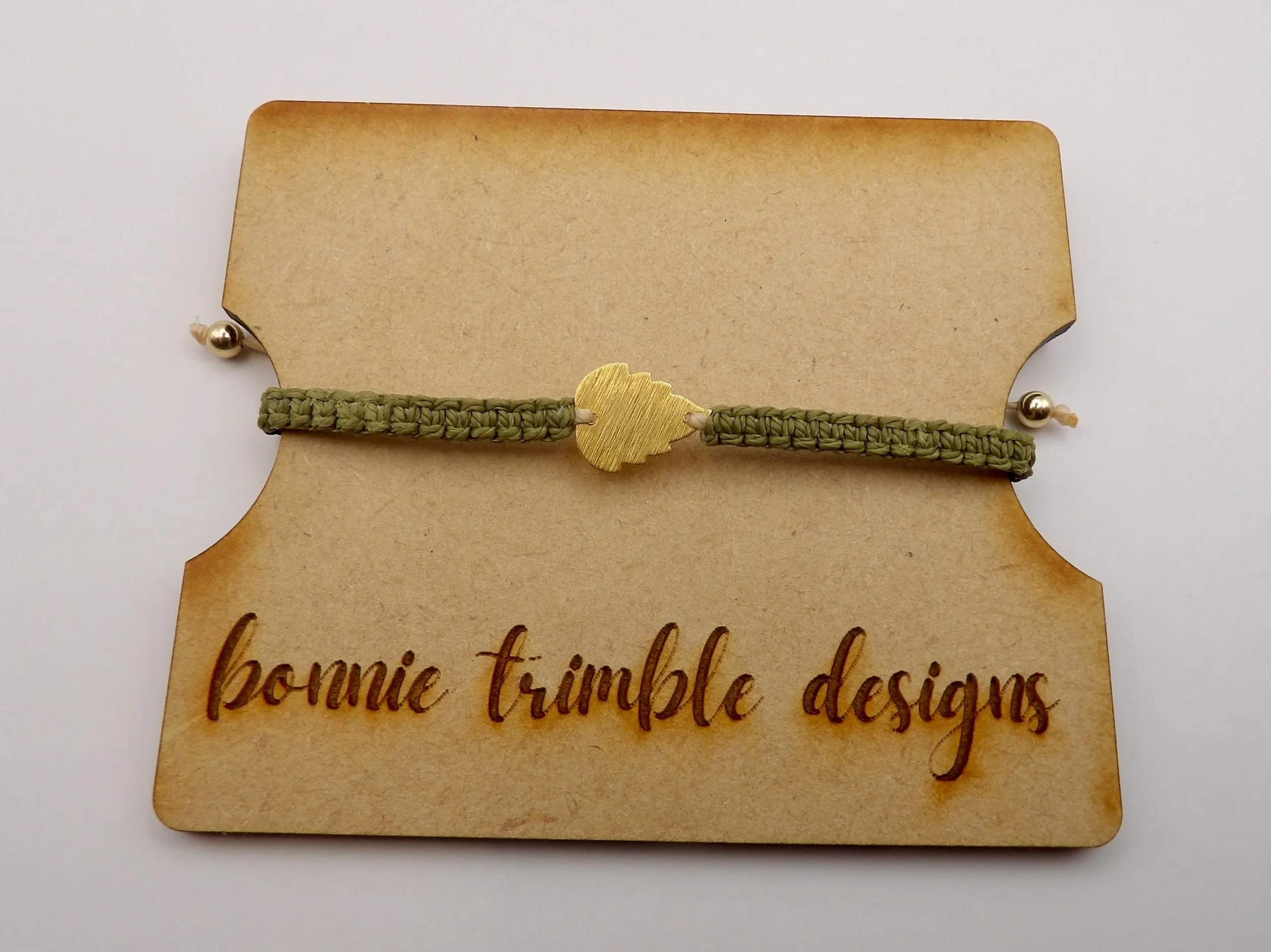 a minimalist botanical cord bracelet showing the intricate twist of the earth-toned macramé band and a satin-finish gold leaf focal.