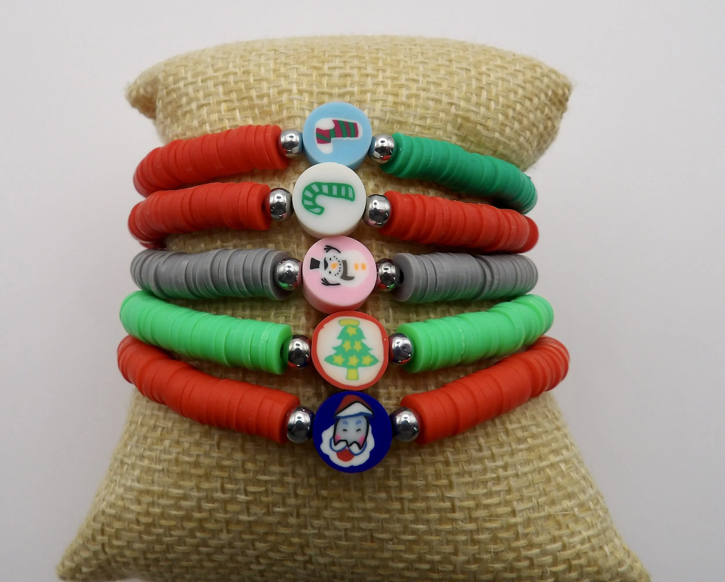 all 5 styles of the handmade christmas polymer clay heishi bracelets, showing the santa, snowman, candy cane, tree, and stocking focal beads.