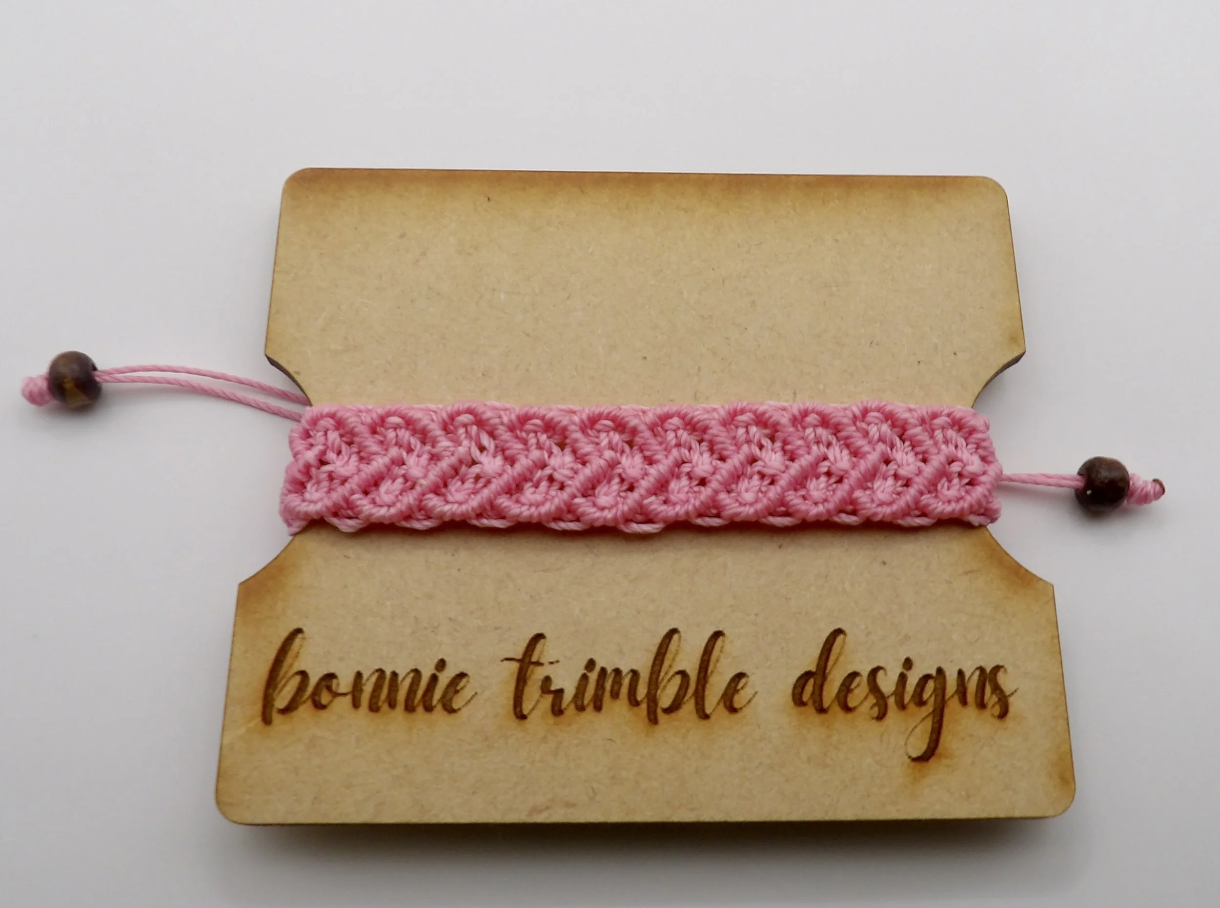 detail view of the dark brown wooden rondelle beads on the adjustable tails of the light pink macrame bracelet.