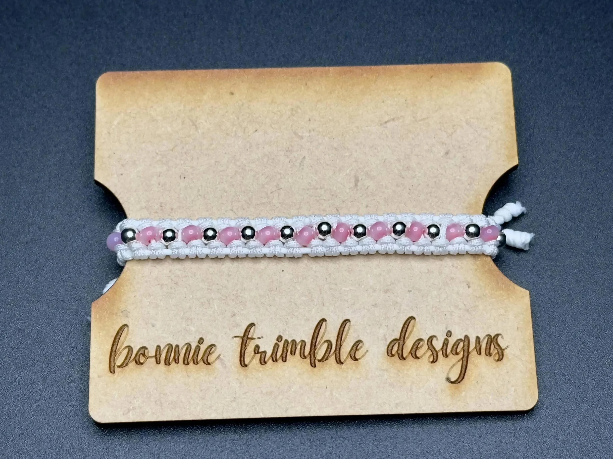 close-up of the detailed dreamer bracelet highlighting the contrast between the crisp white cord and the tiny pink bead details.