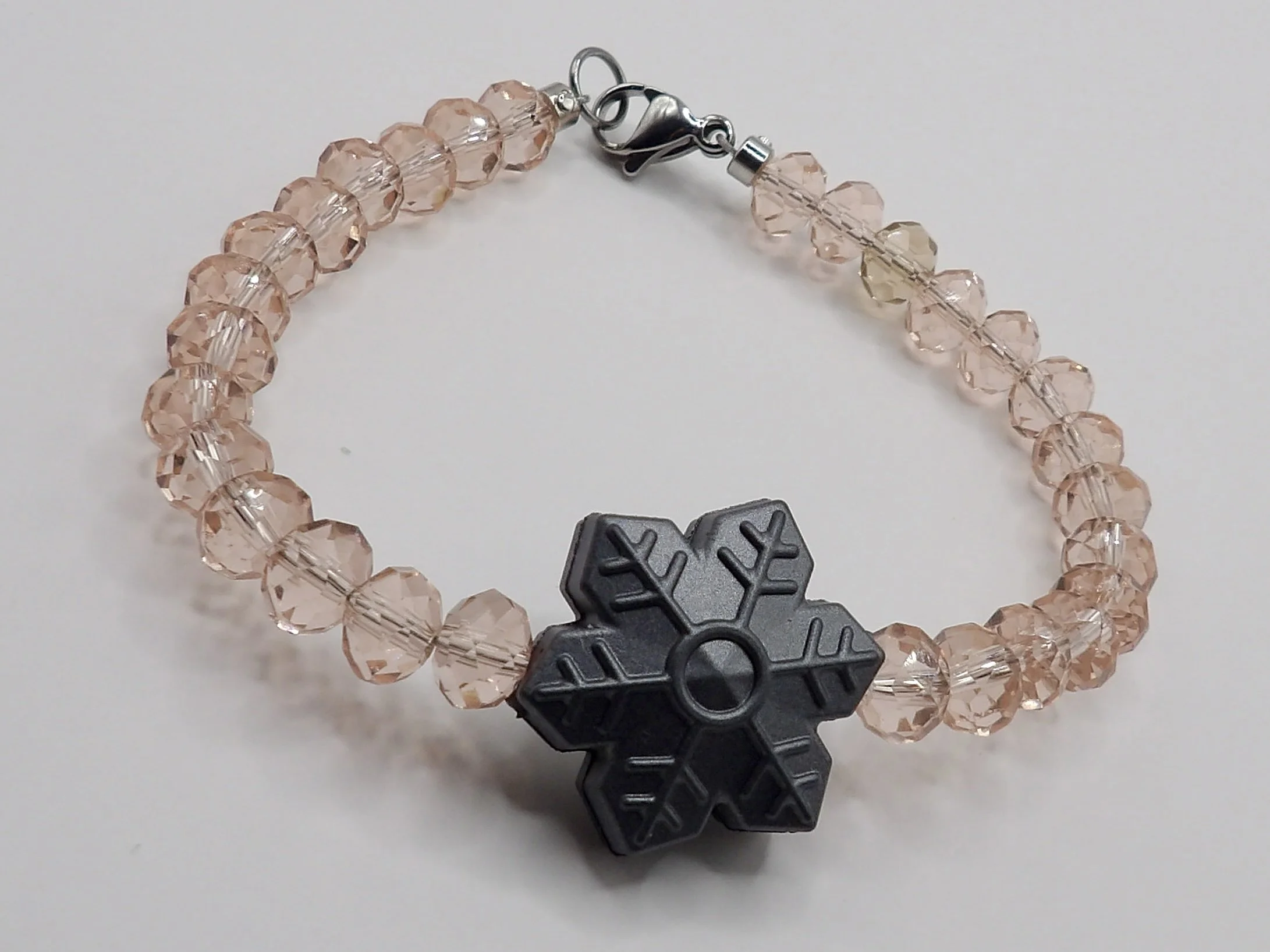 handmade holiday bracelet with clear pink faceted glass beads, a metallic silver silicone snowflake charm, and stainless steel clasp.