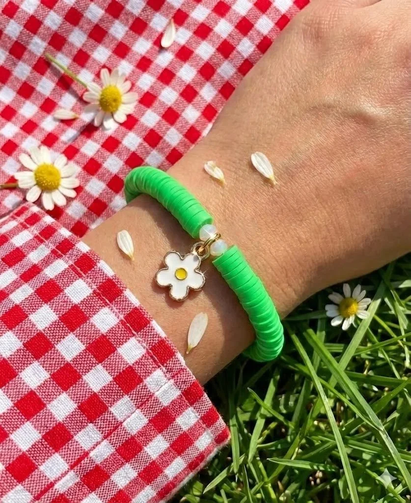 green polymer clay heishi bracelet on a wrist with a gold daisy charm and sparkling crystal spacers.
