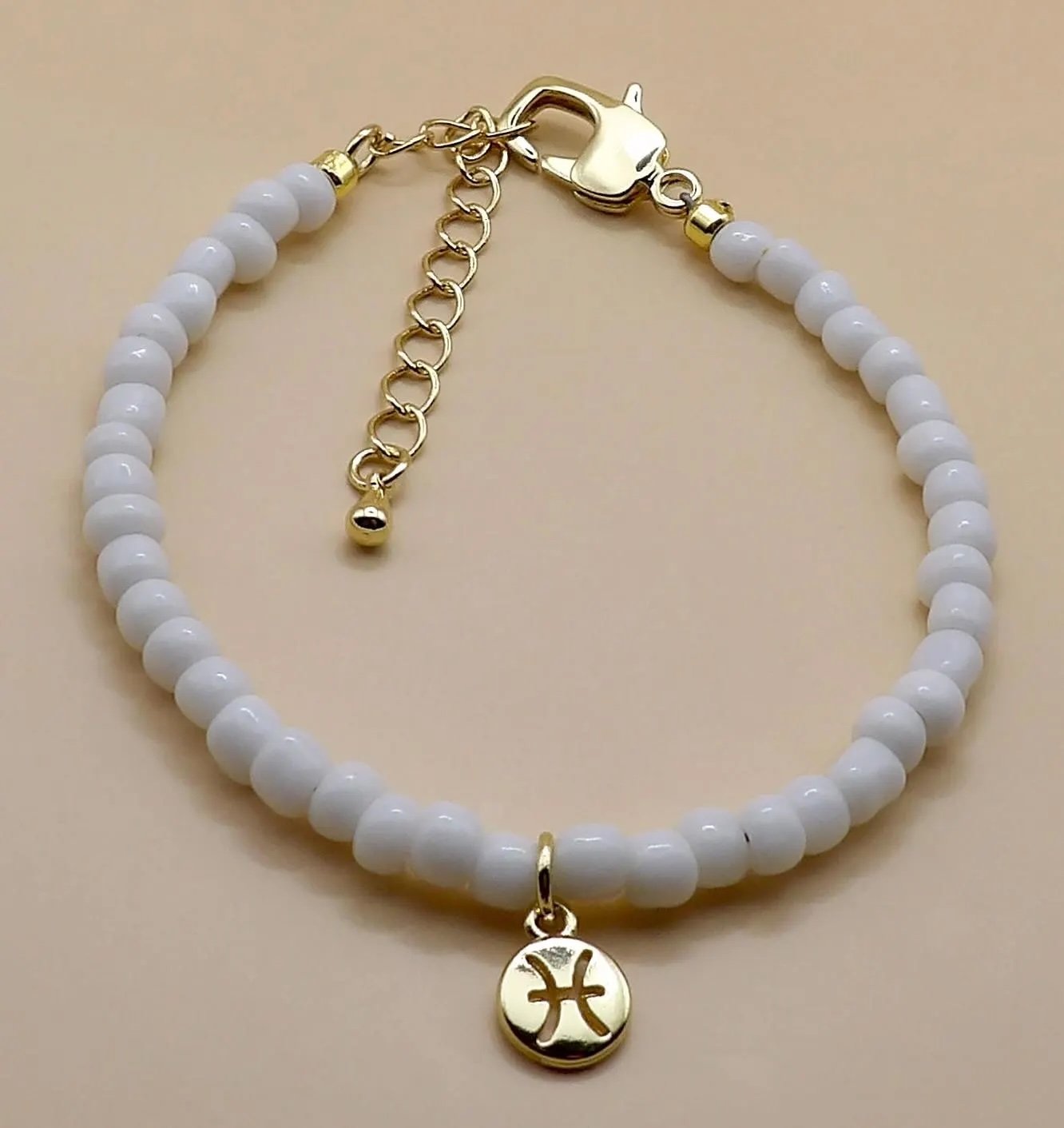 the celestial dreamer bracelet highlighting the intricate detail of the gold-plated zodiac charm and white bead accents.