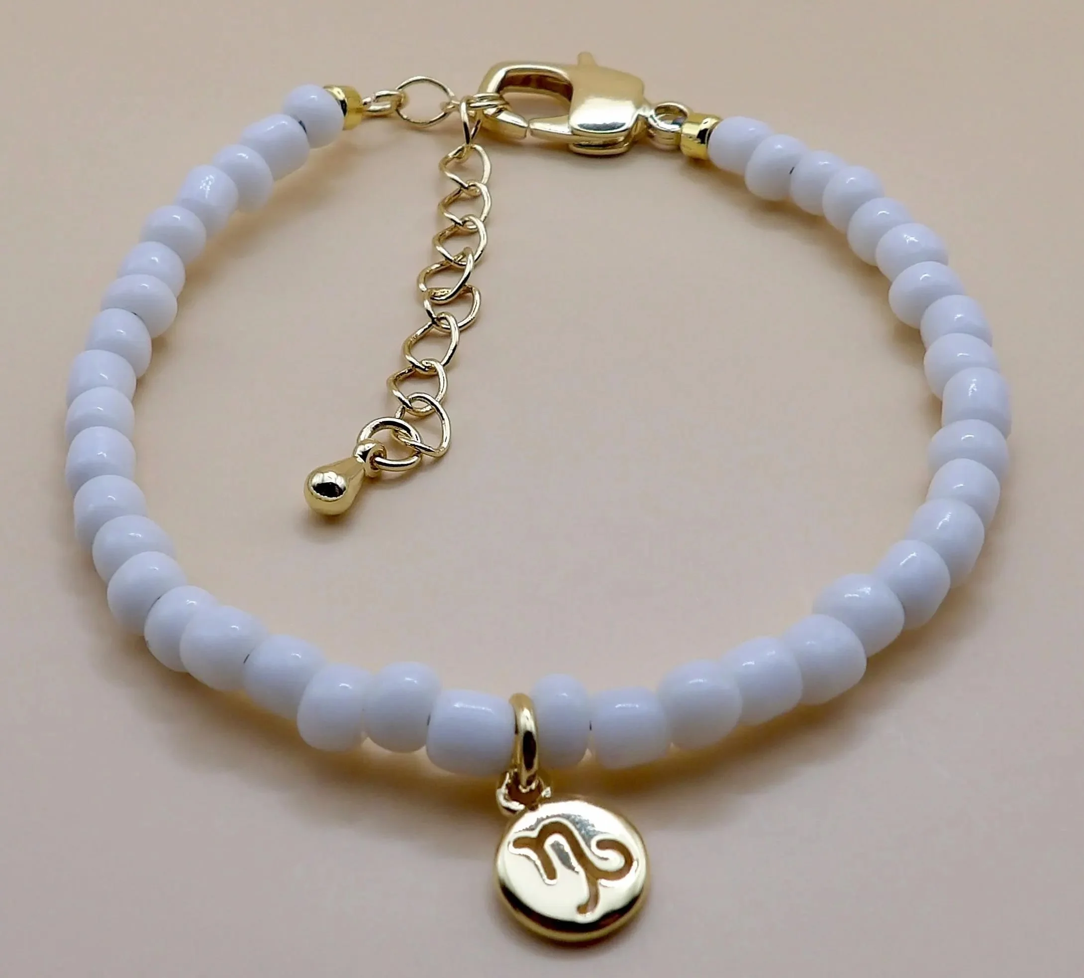 white seed bead strand with a central 18k gold plated zodiac charm, styled for a celestial-themed stack.