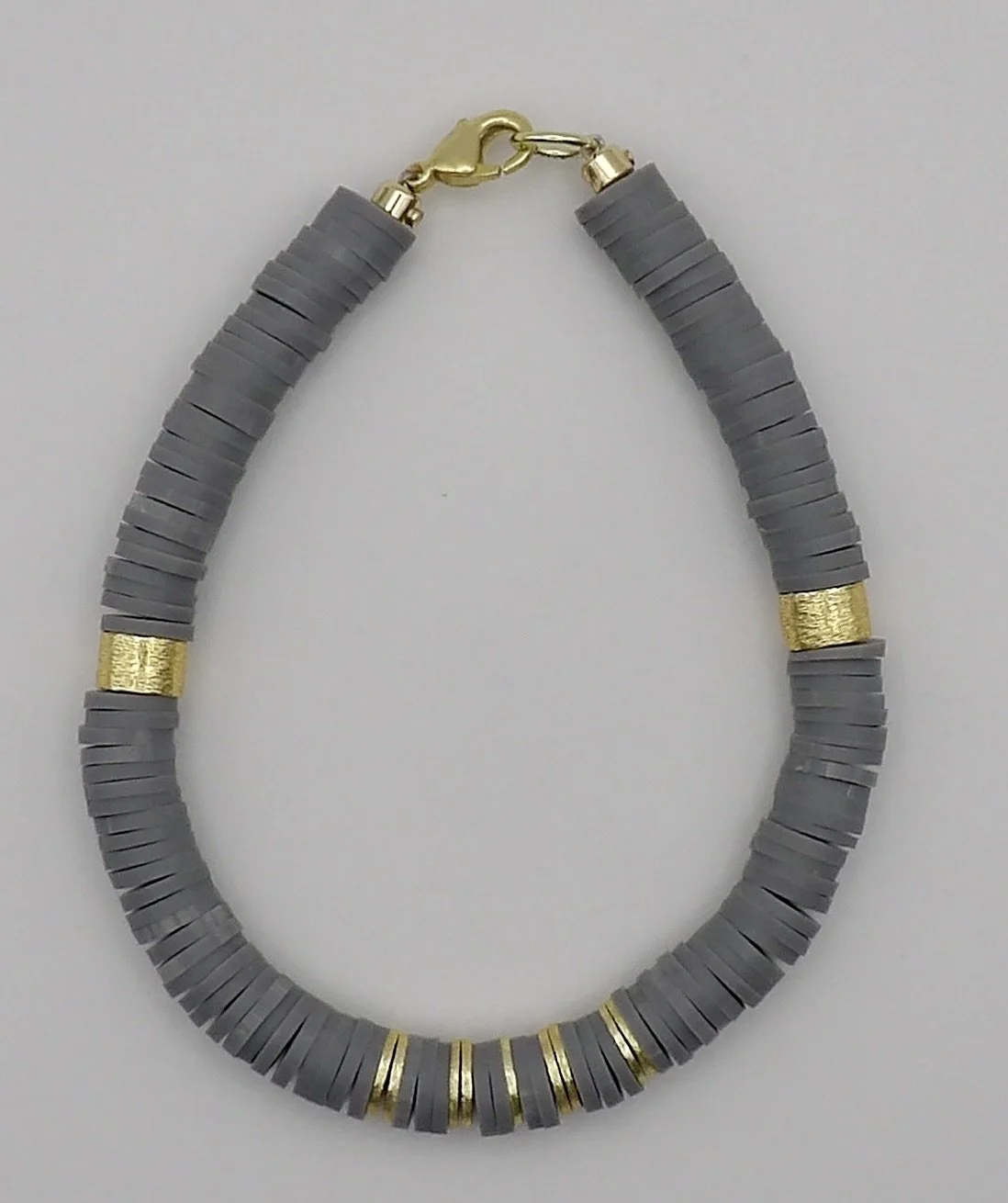detail view of the back of the bracelet, showing the 14k solid gold brushed drum-shaped bead accent on the gray heishi band.