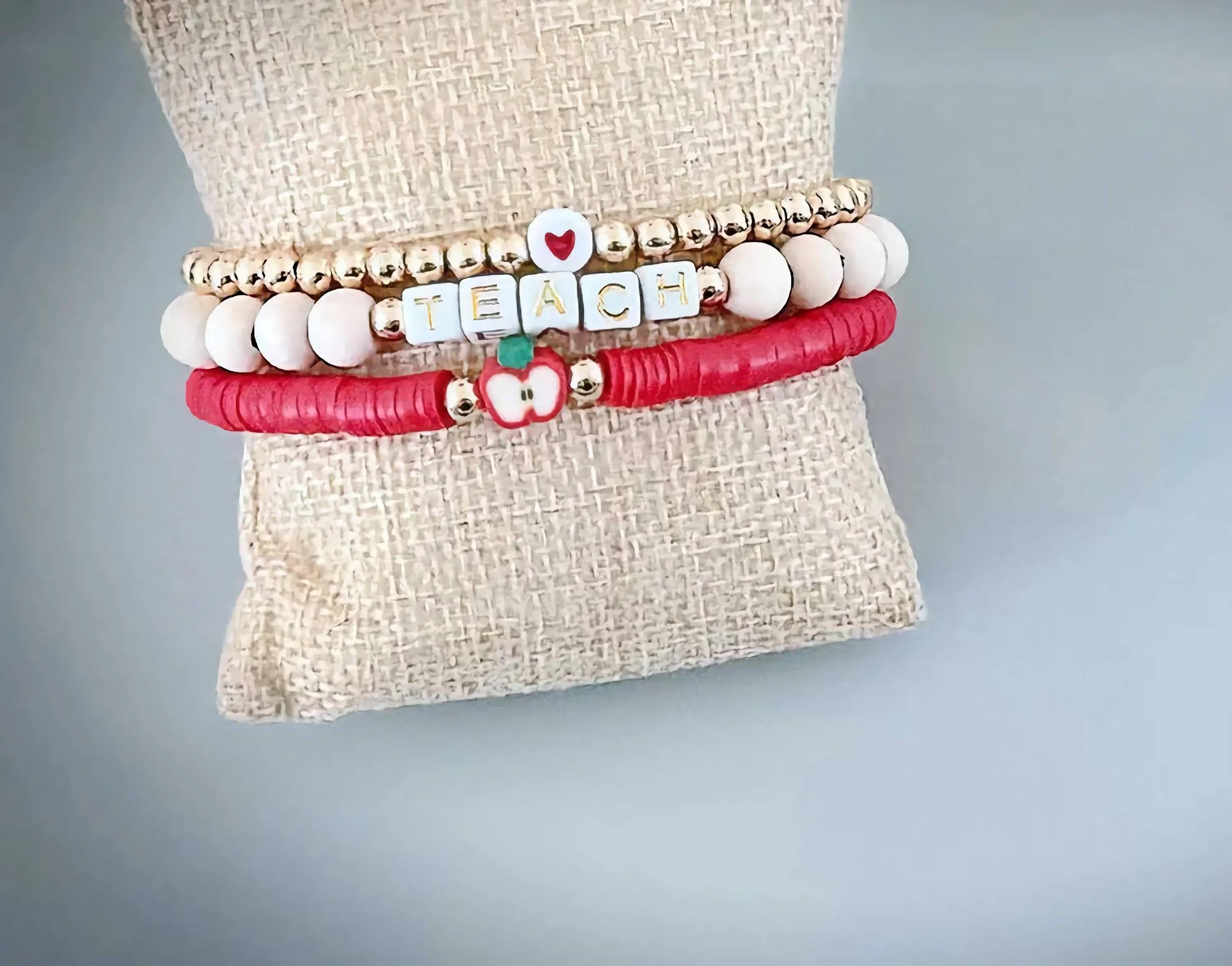 18k gold plated teacher bracelet set with a red apple charm and "teach" word beads draped over a real red apple as a sentimental gift prop.